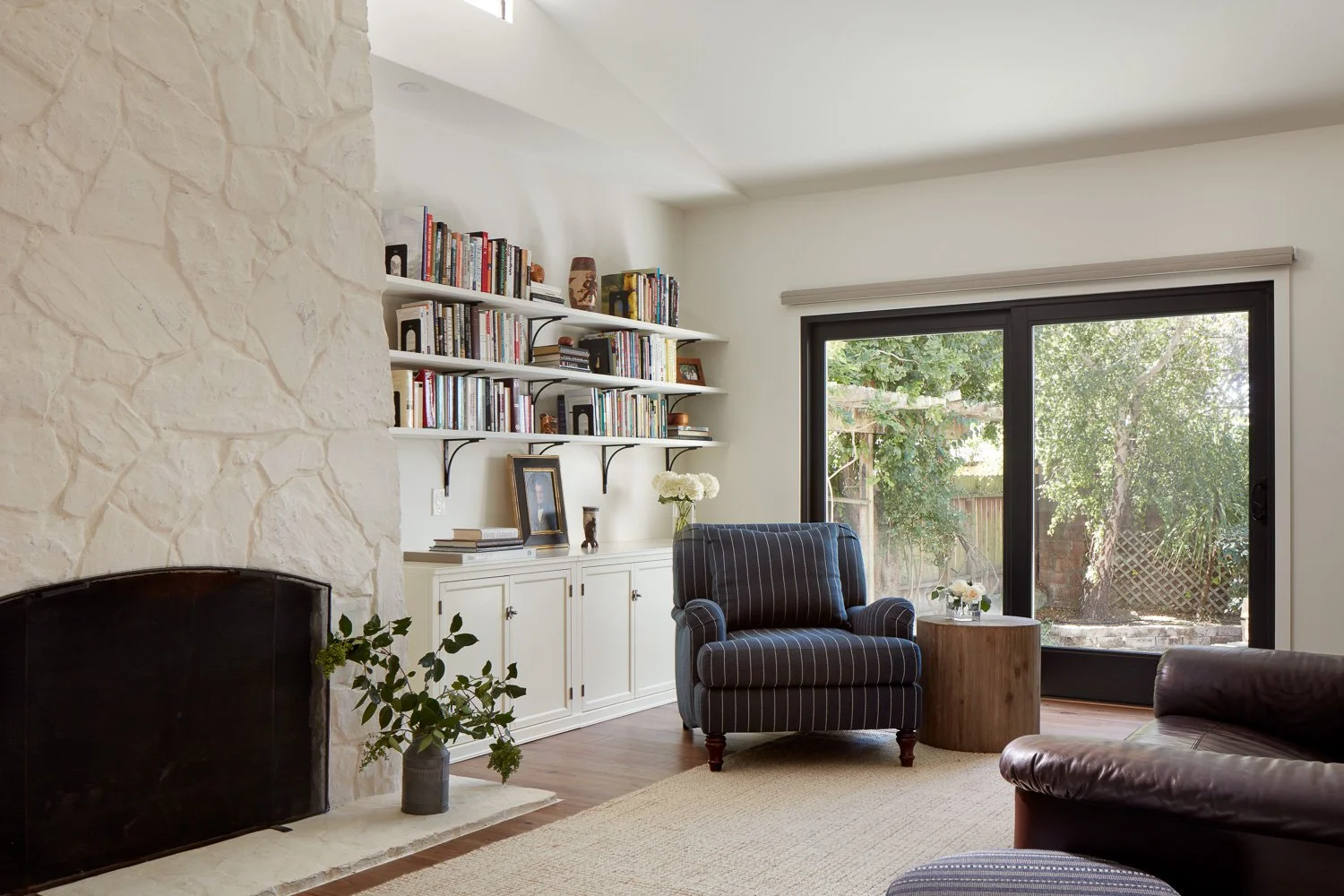 Cozy family room with stone fireplace, custom shelving, lounge seating, and sliding doors opening to the backyard.