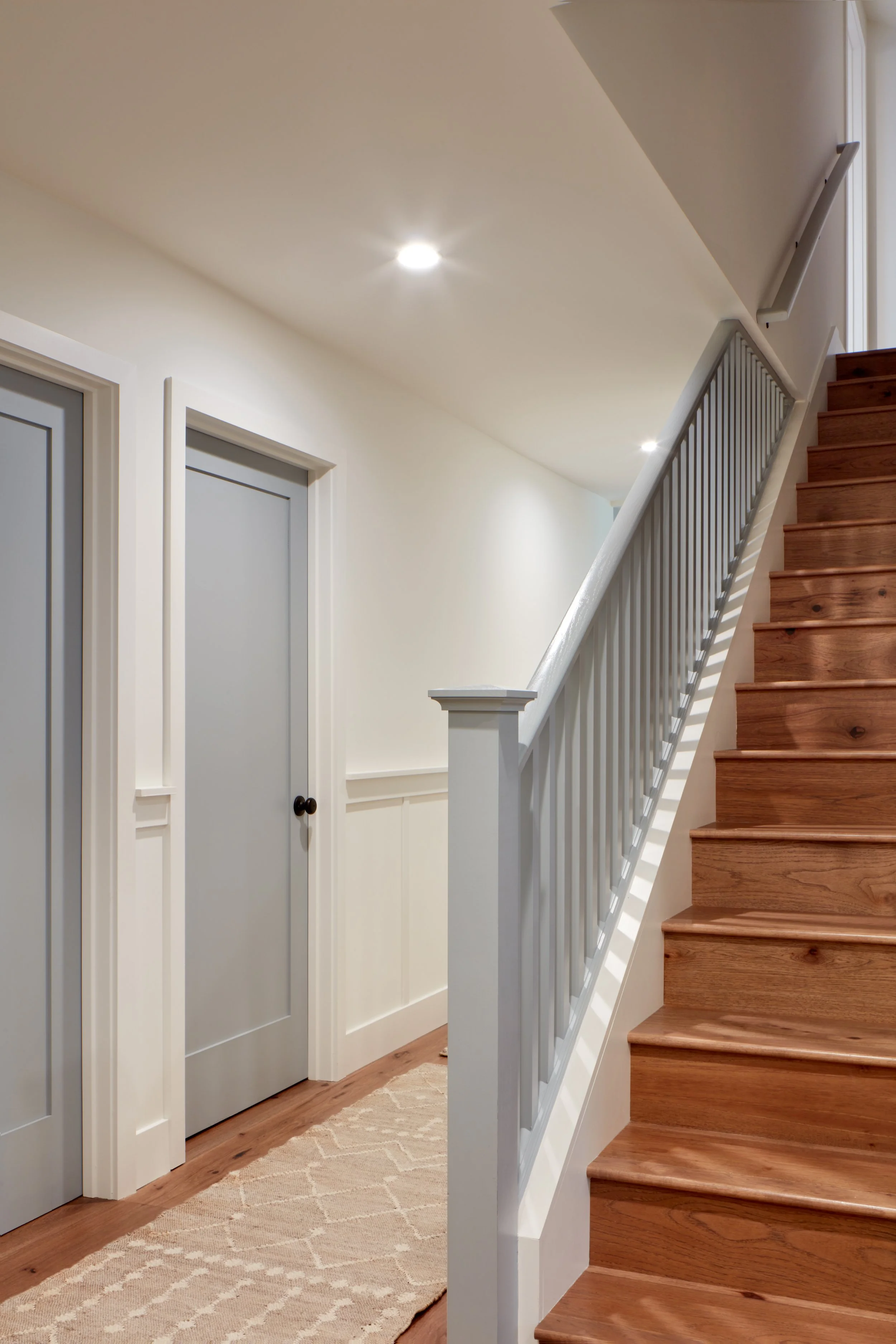 Modern Pacifica home remodel hallway featuring wood staircase, white wainscoting, and warm hardwood floors