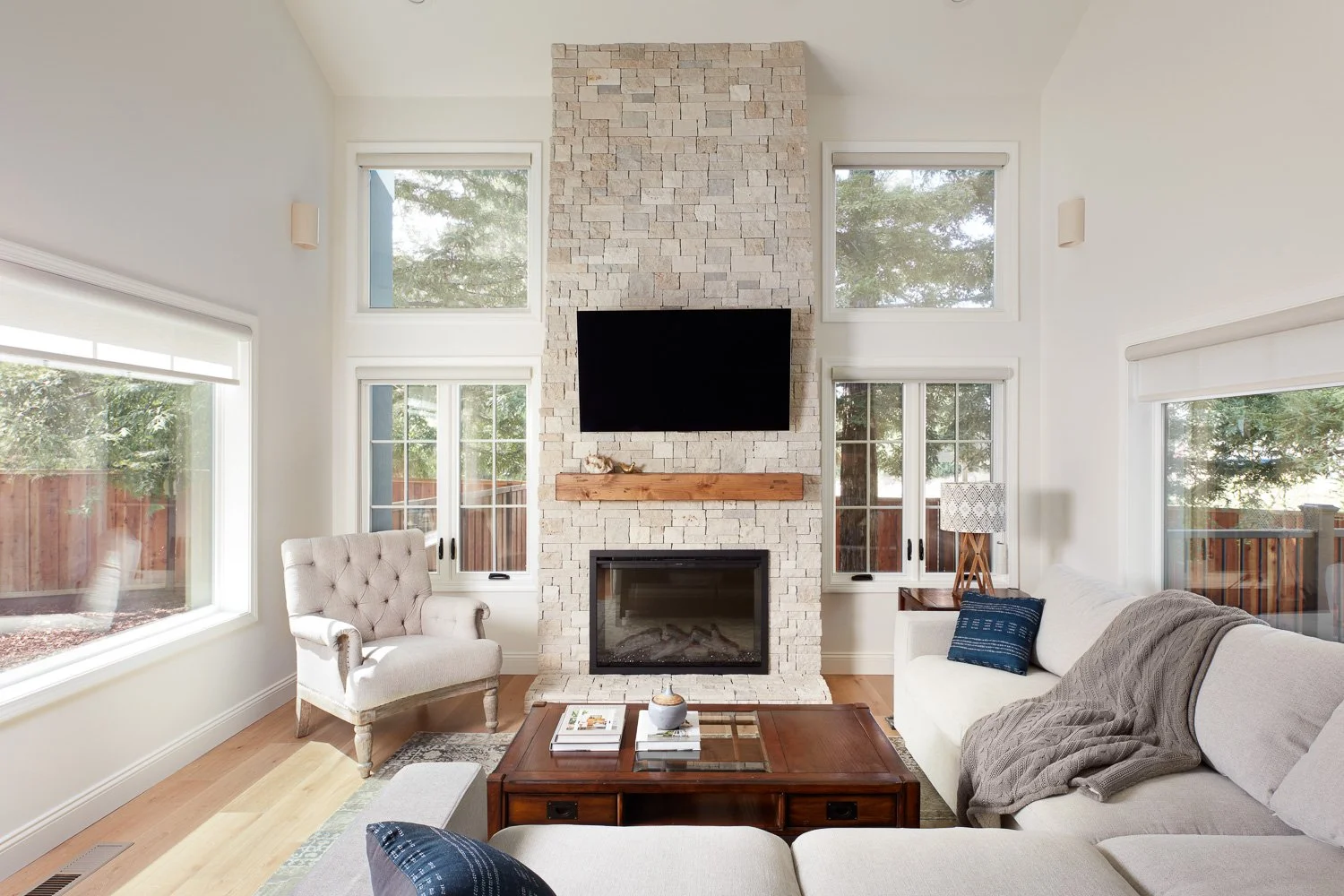 Bright living room with stone fireplace and tall windows – custom home remodel.
