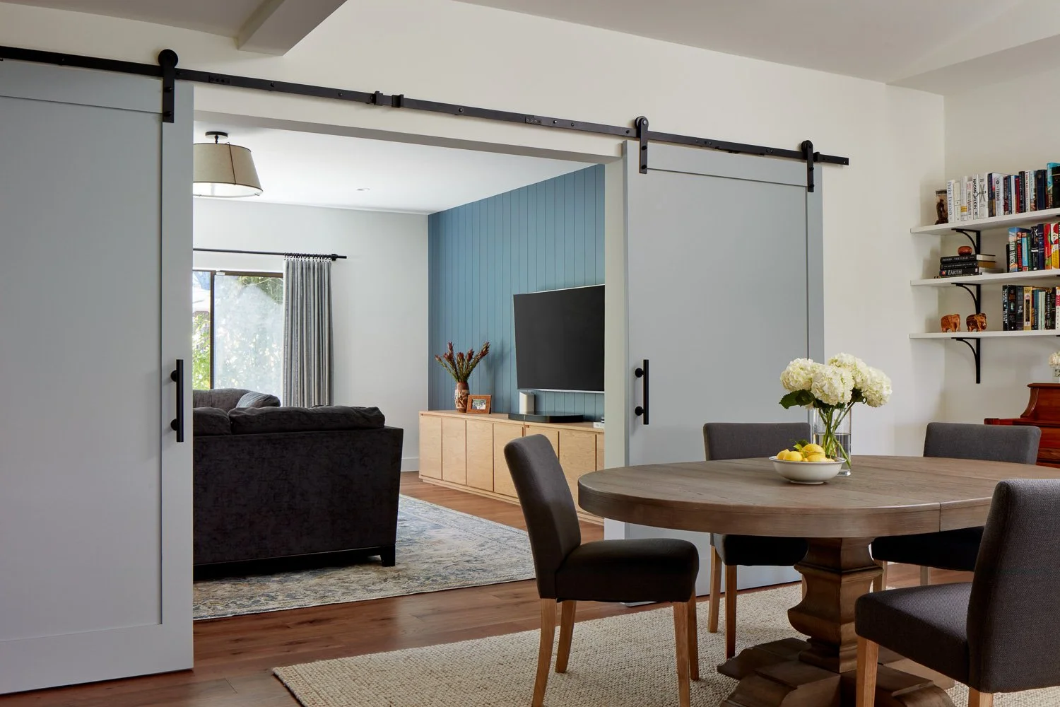 Open dining and living space with sliding barn doors, round wood table, and seamless flow between rooms.