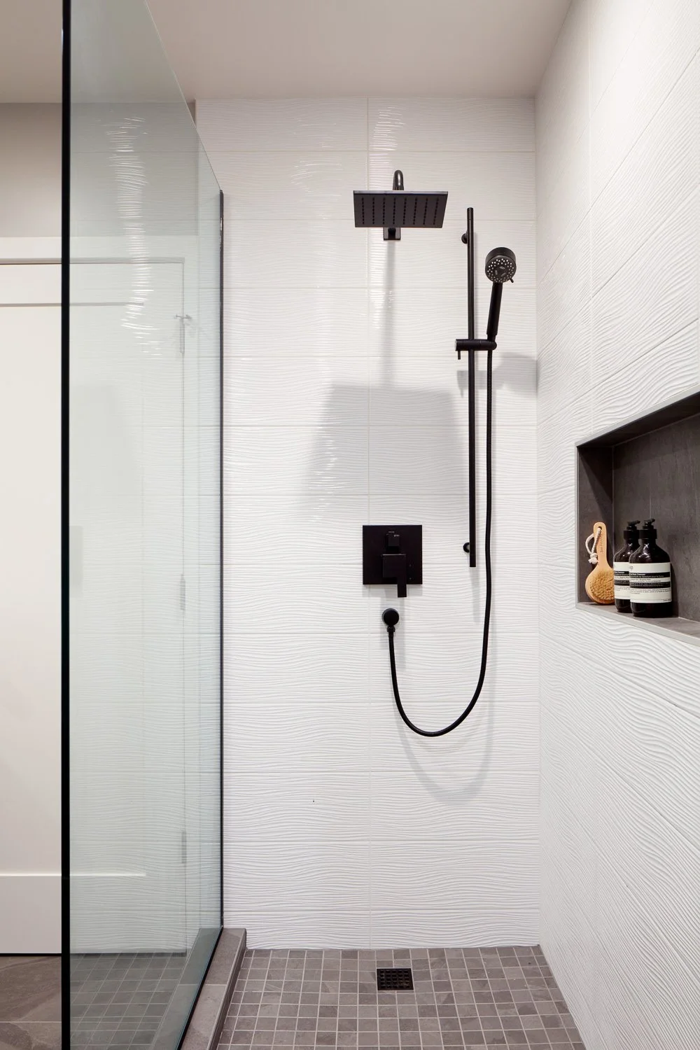 Modern black fixtures and textured tile create a refined shower design within this luxury new construction home.