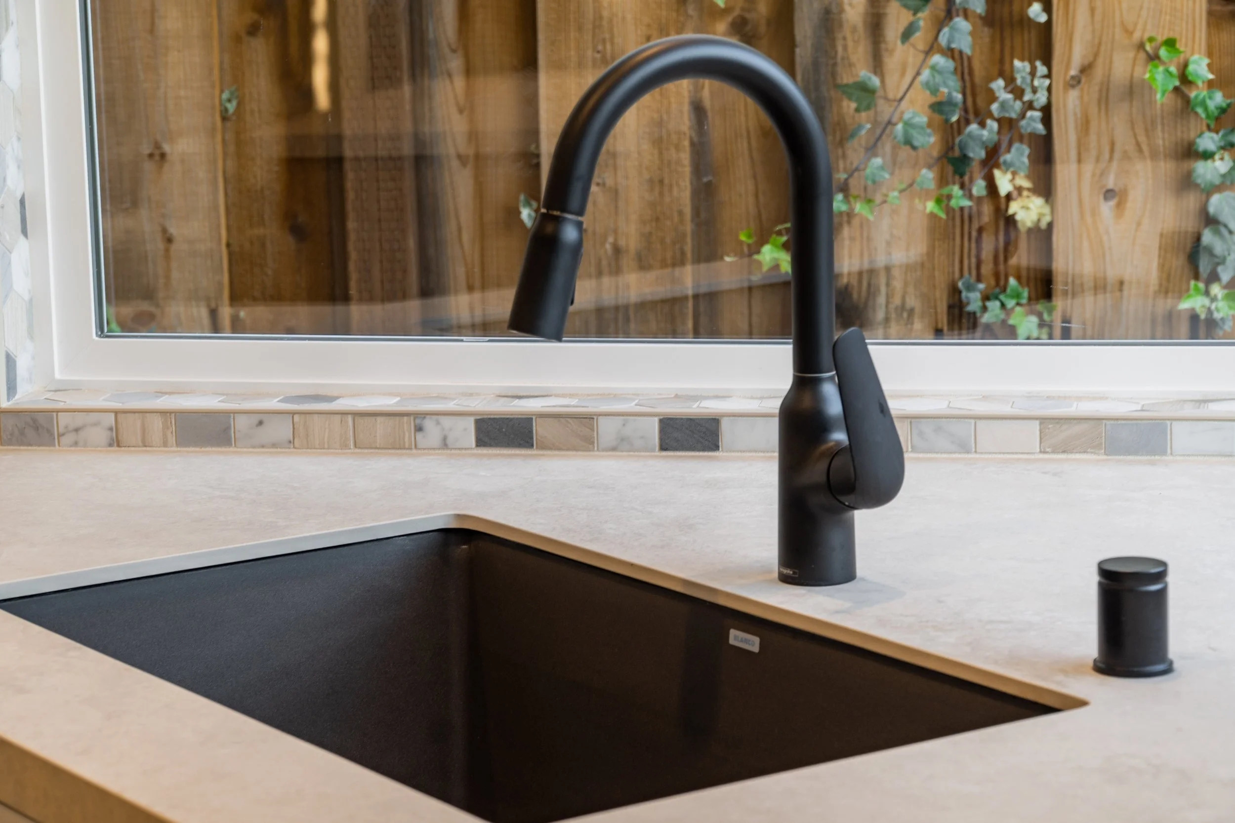 Matte black kitchen faucet over an undermount sink with patterned tile detail beneath the window.