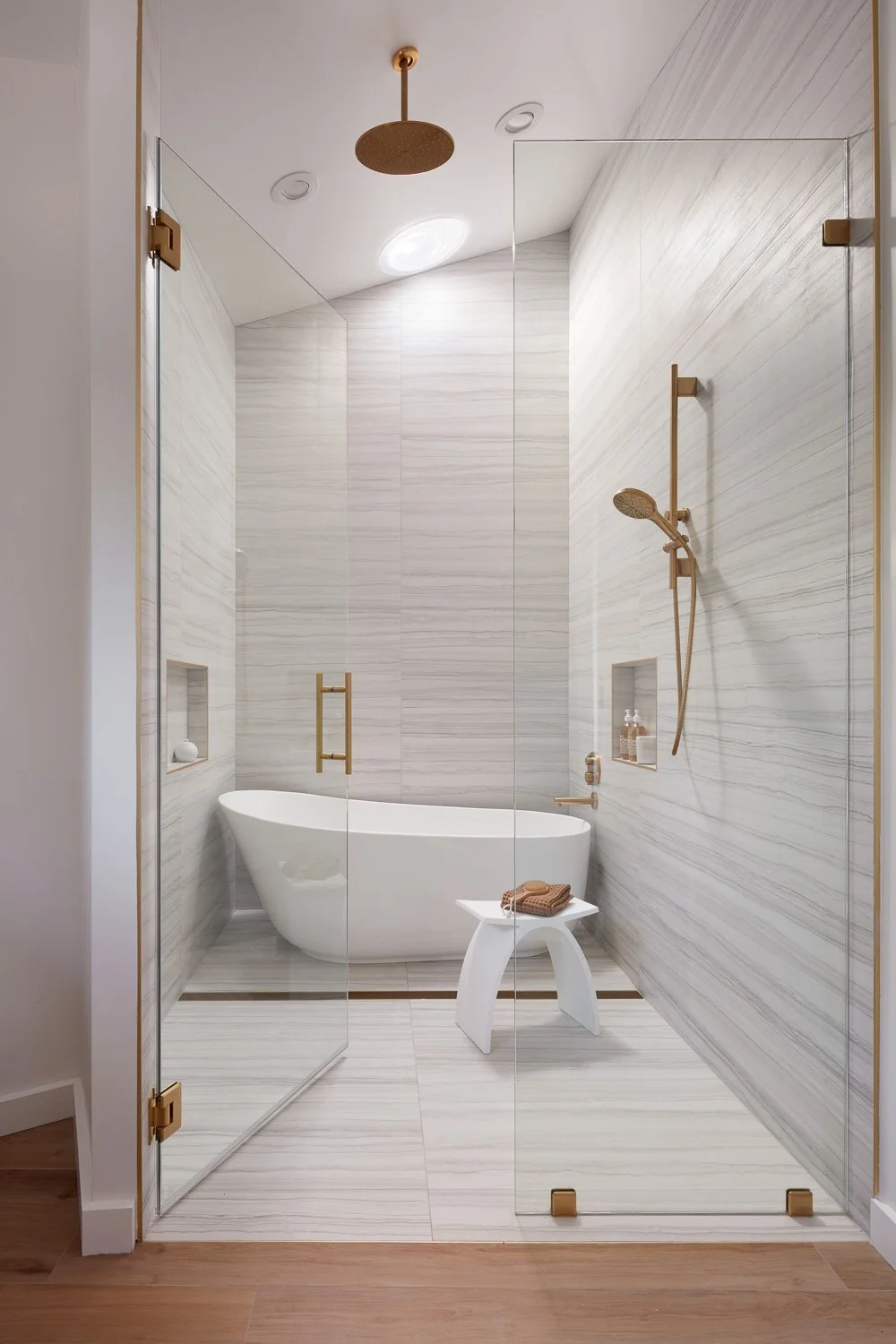 Spa-inspired primary bath with a freestanding tub, full-height stone tile, and warm brass fixtures.