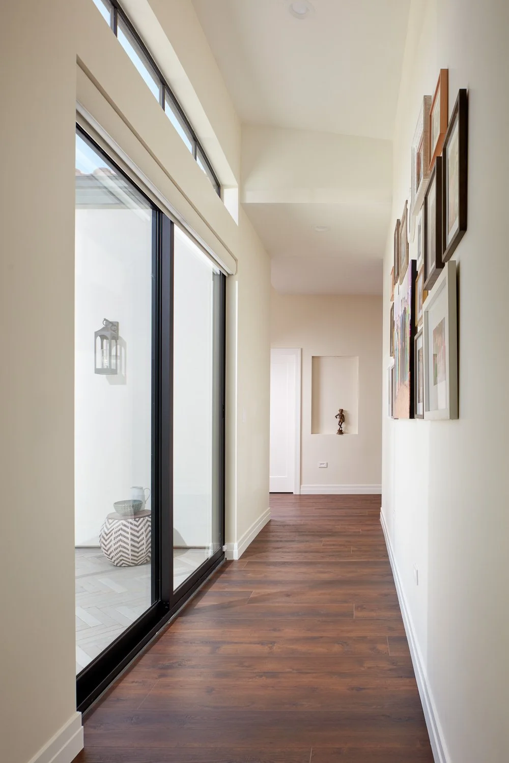 Bright, inviting hallway featuring expansive windows, warm wood flooring, and a curated gallery wall for a modern, welcoming feel.