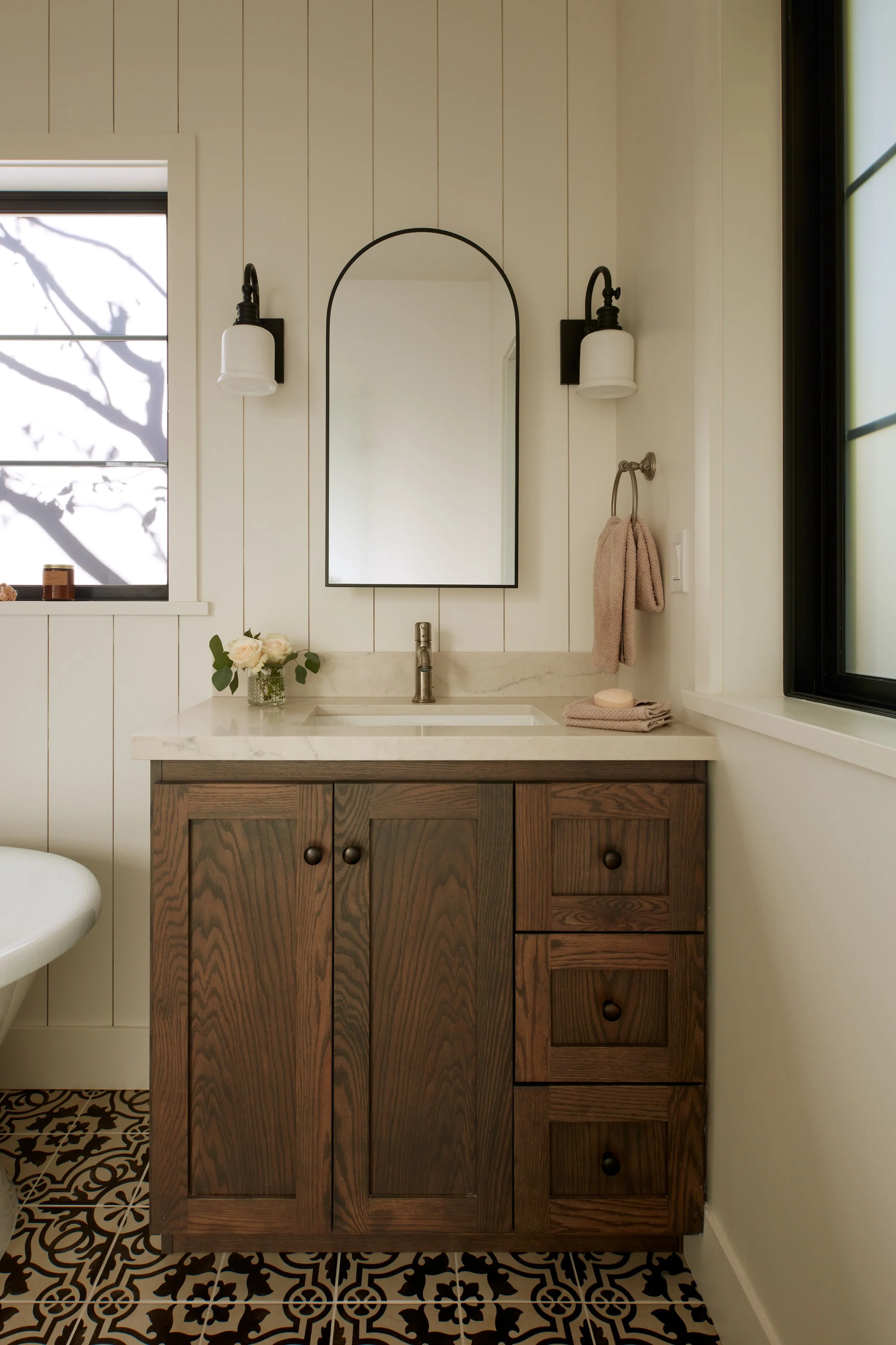 Custom wood bathroom vanity with stone countertop, arched mirror, and patterned tile flooring in Pacifica luxury remodel