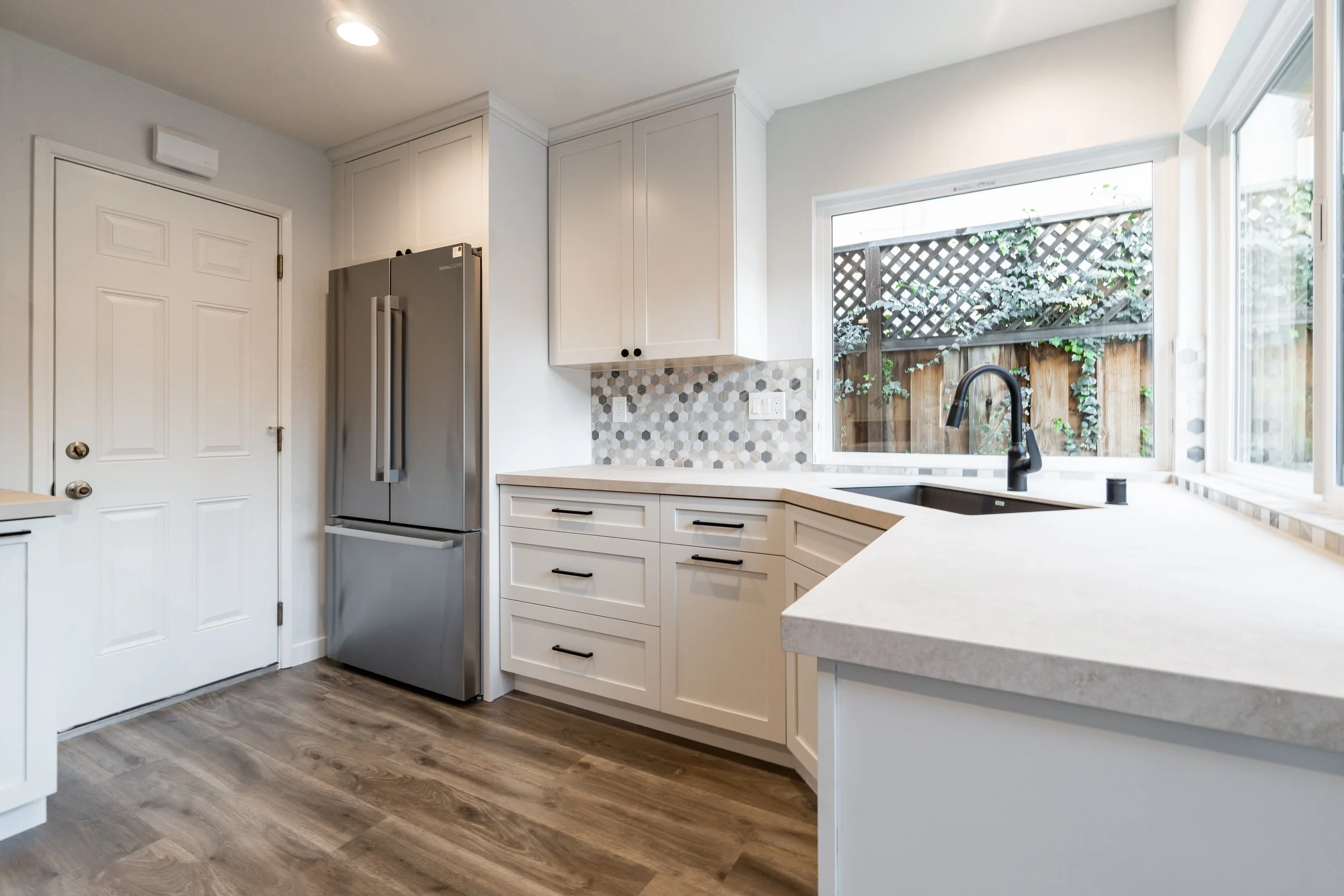 Modern kitchen with white shaker cabinets, stainless refrigerator, and wood-look flooring.