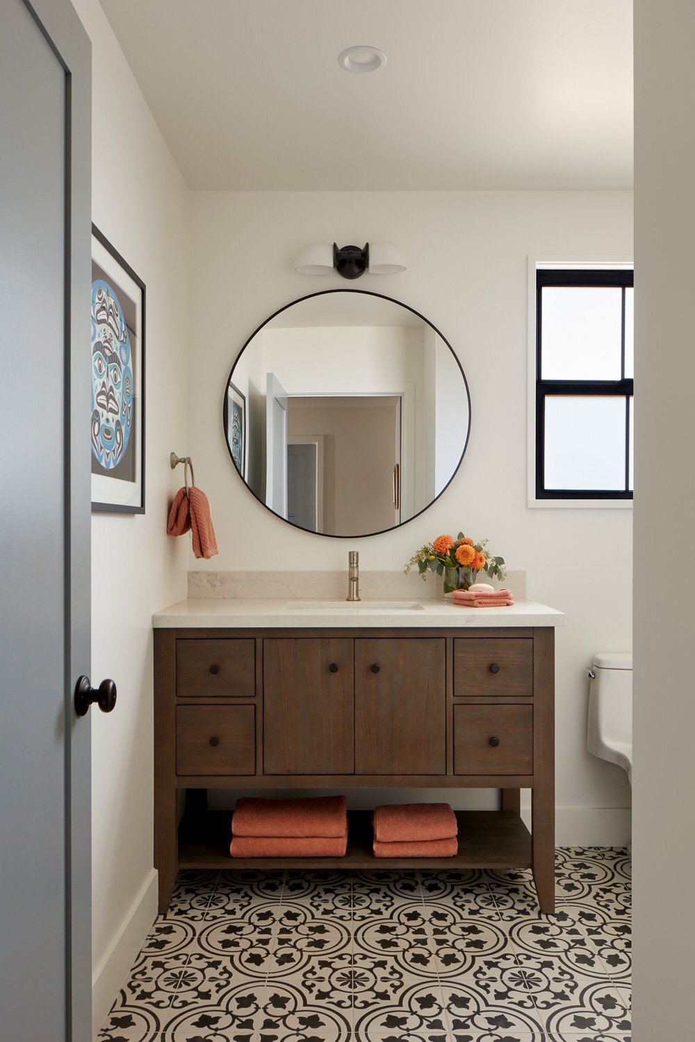 Modern bathroom vanity with round mirror, patterned tile flooring, and warm wood cabinetry in Pacifica home remodel.