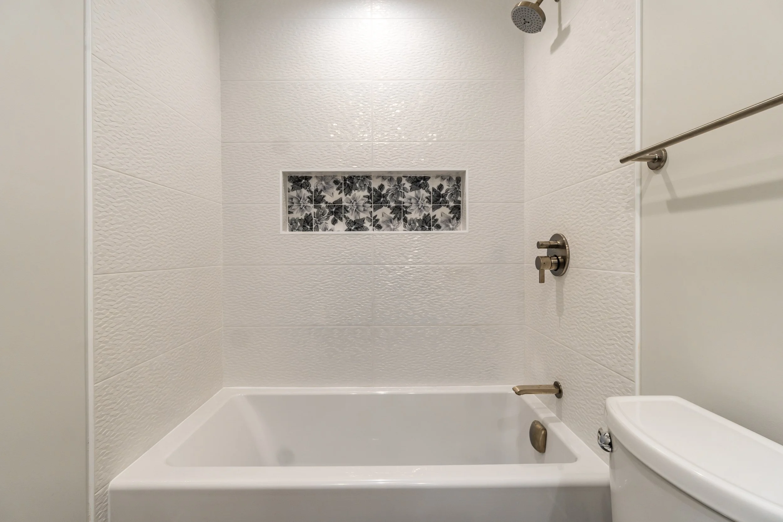 Clean white tub-shower combo with textured tile walls and decorative niche accent.