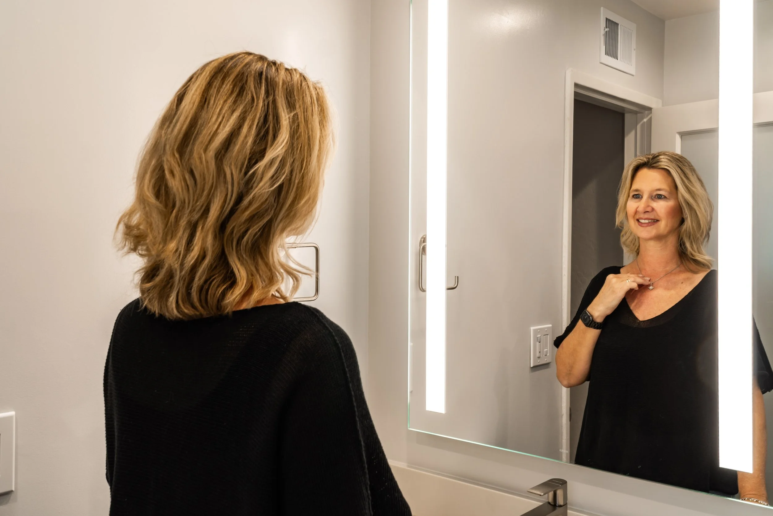 Project designer Petra admiring the finished bathroom, reflected in a modern LED-lit mirror during a San Jose home remodel.