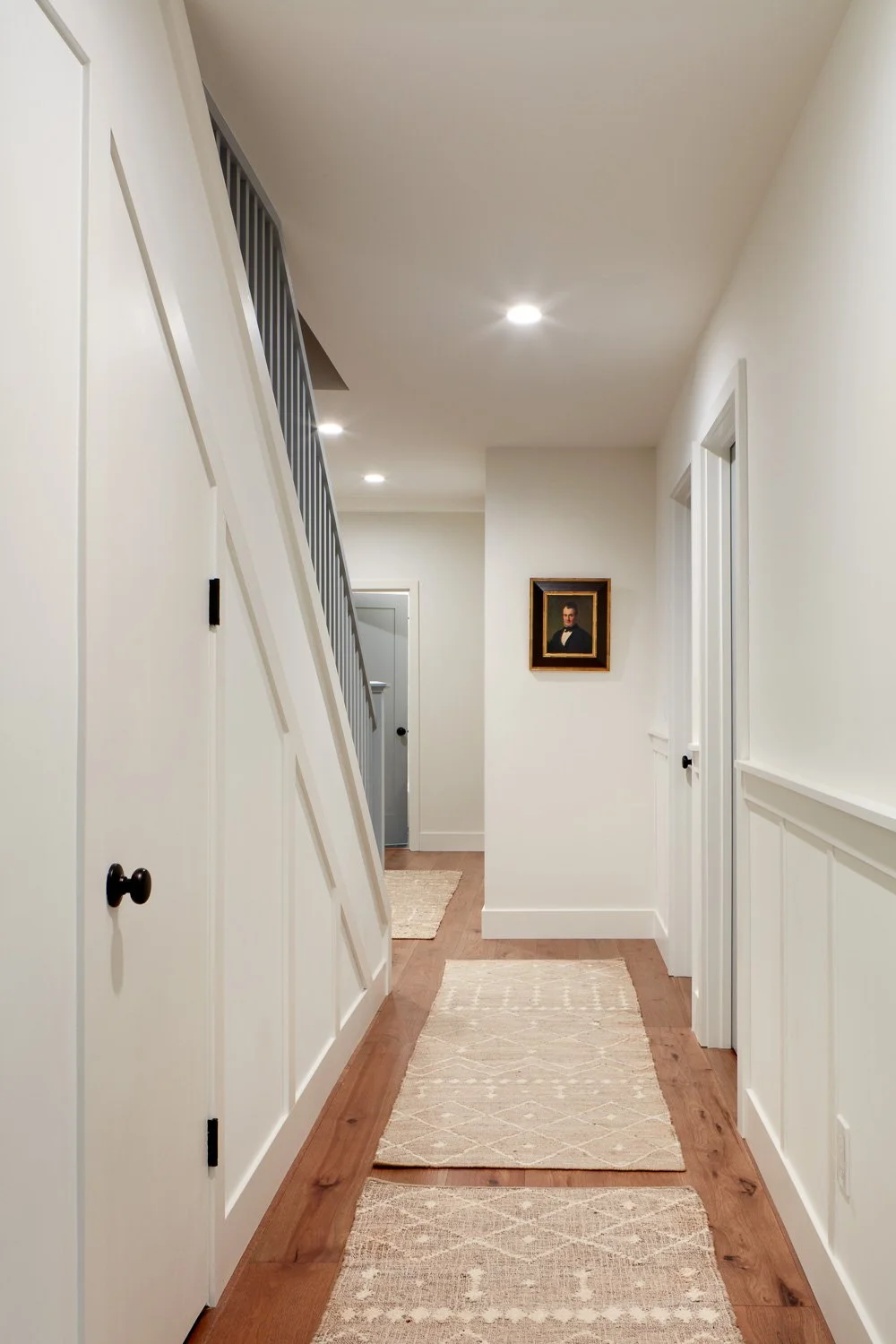Bright hallway remodel with wood flooring, modern doors, wainscoting, and recessed lighting in Pacifica home.