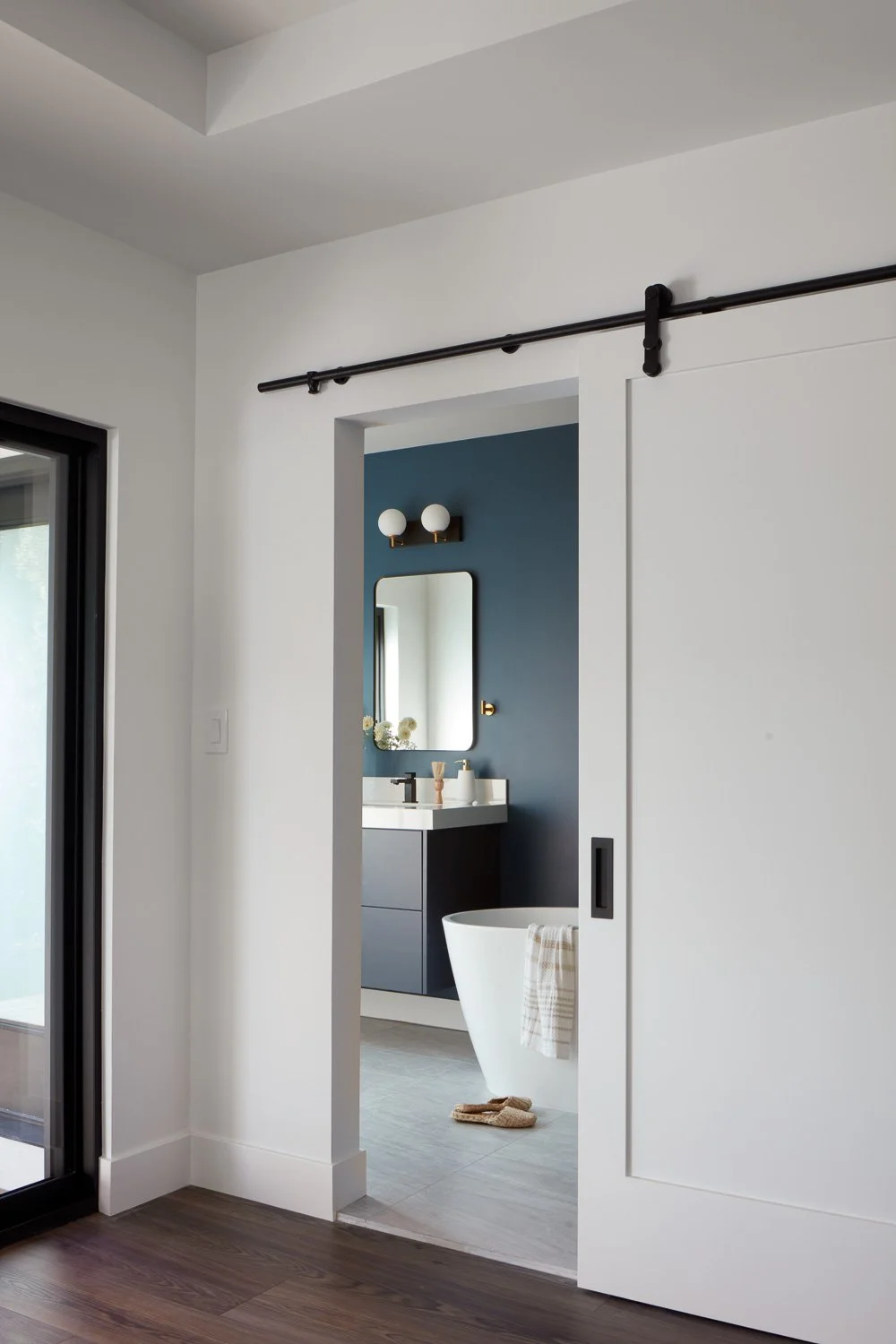 A sliding barn door creates a seamless transition into the primary bath, blending function and design in this new construction home.
