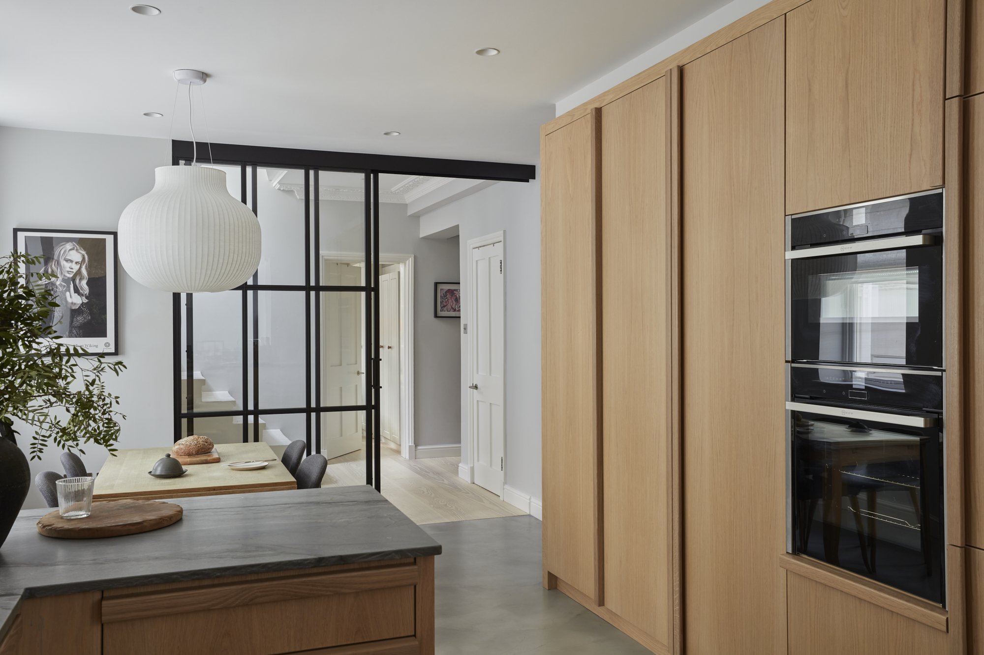 Modern kitchen and dining area with wooden cabinets, built-in ovens, dining table with chairs, and decorative artwork on the wall.