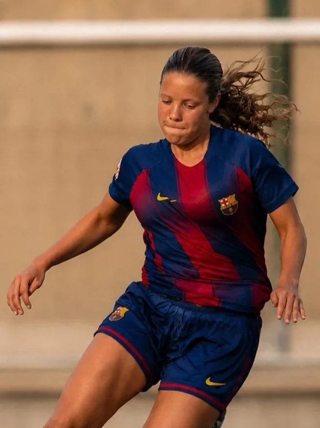 Joven jugadora de fútbol con uniforme del FC Barcelona en un campo de fútbol.