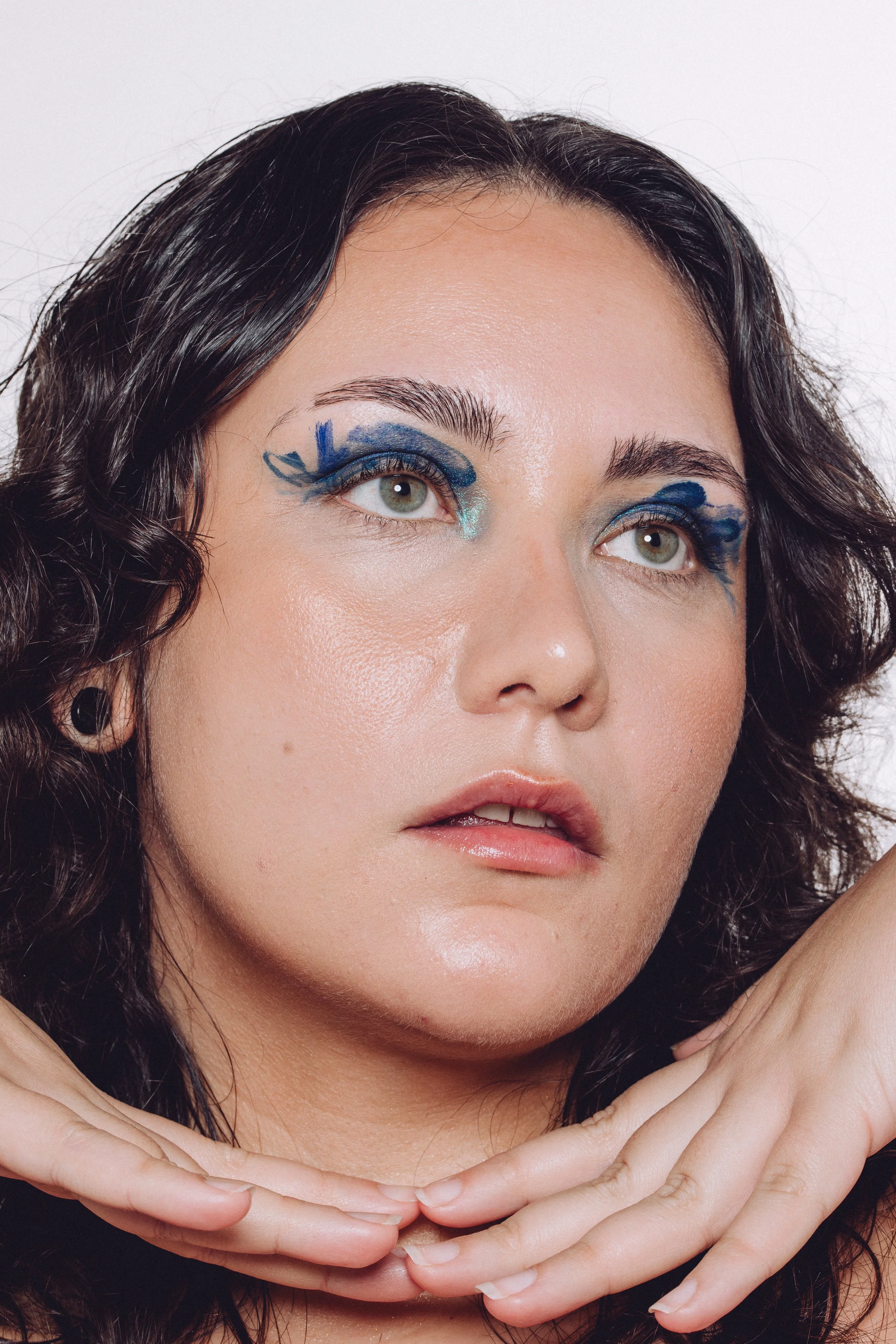 Close-up portrait of a woman with dark curly hair and artistic blue eye makeup.