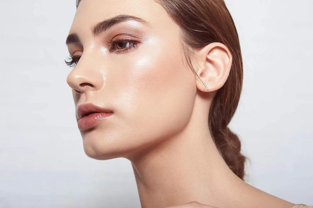 Close-up of a woman with clear skin, light makeup, and brown hair tied back, looking to the side.