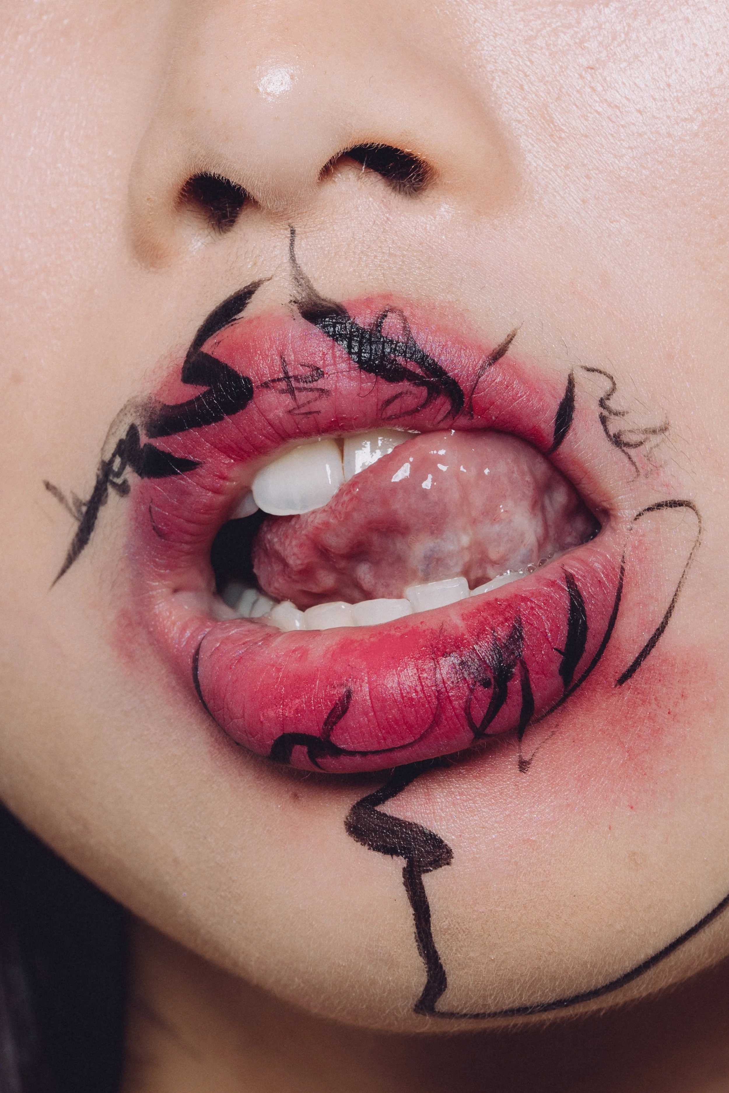 Close-up of a person’s lips with artistic black line drawings on the lips and surrounding skin, holding a tongue out.