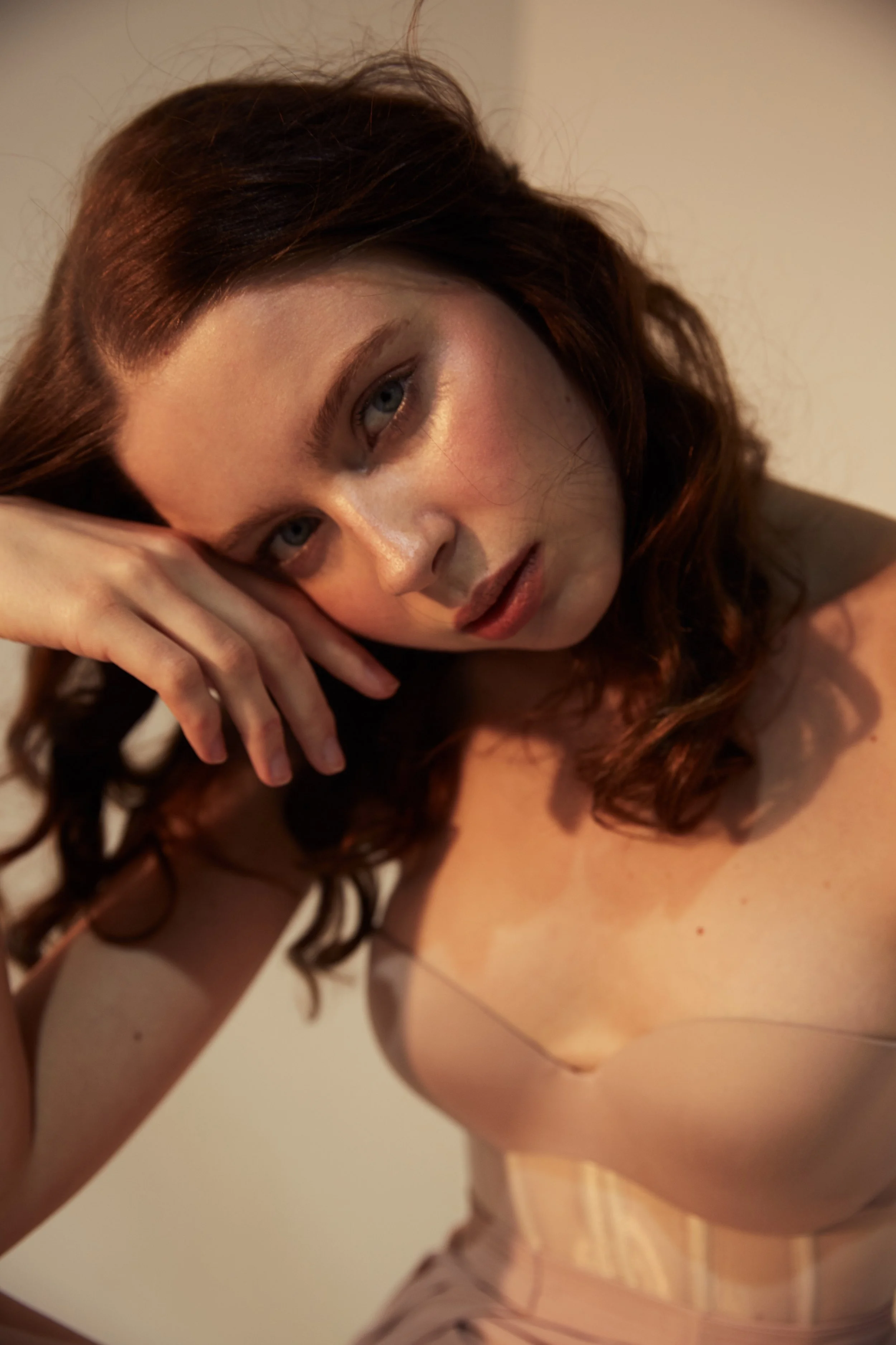 A woman with wavy, reddish-brown hair resting her head on her hand, looking at the camera.
