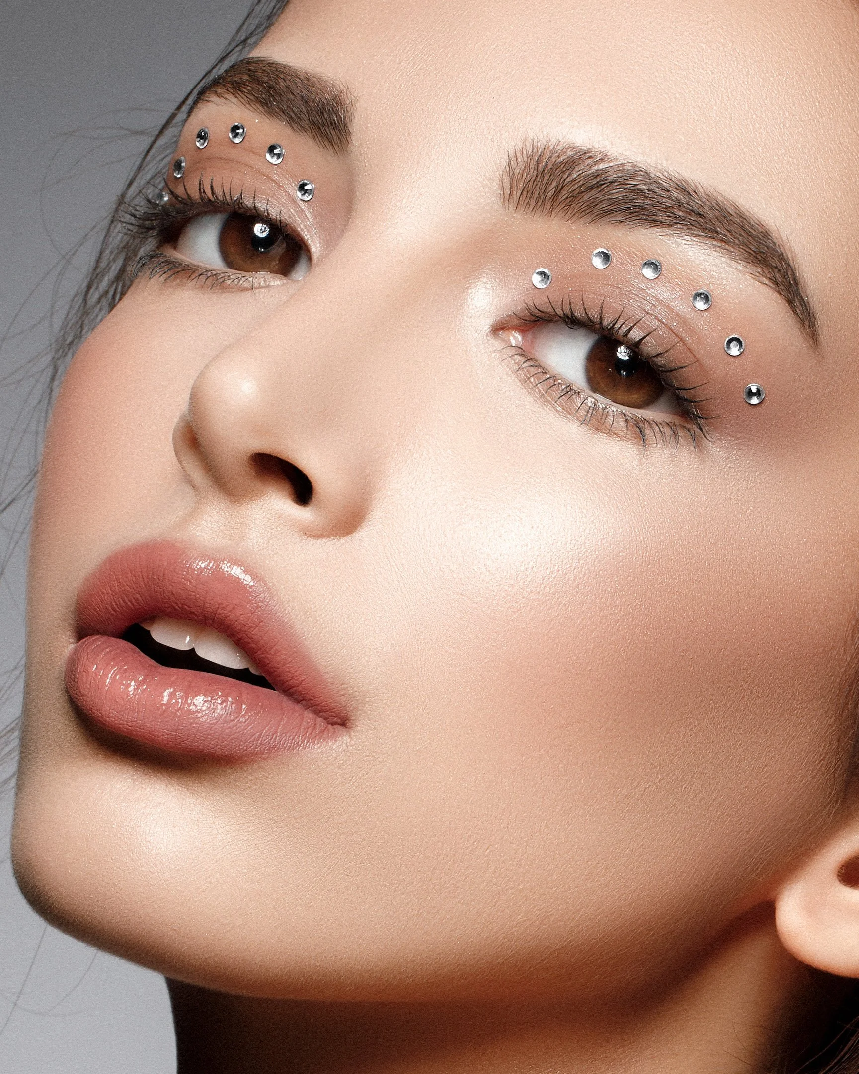 Close-up of a woman's face with makeup and rhinestones above her eyebrows.