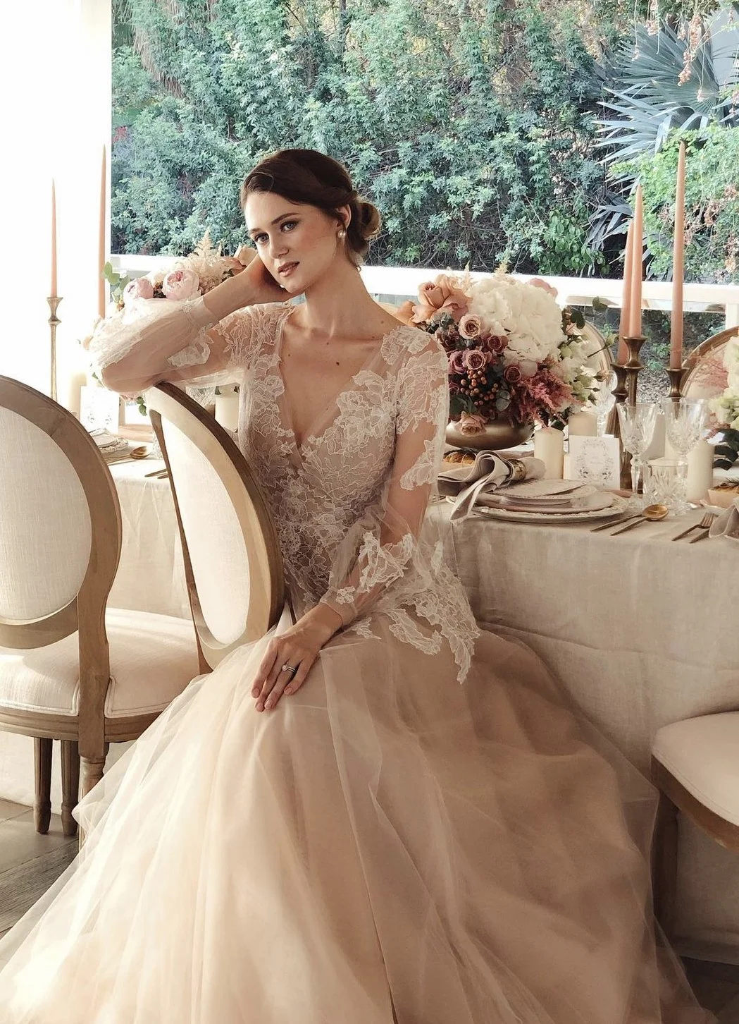 A woman in a lace wedding dress sitting at a decorated table with flower arrangements and candles