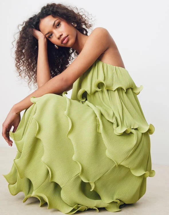 Woman with curly hair sitting and resting her head on her hand, wearing a bright yellow ruffled dress with swirling frills.