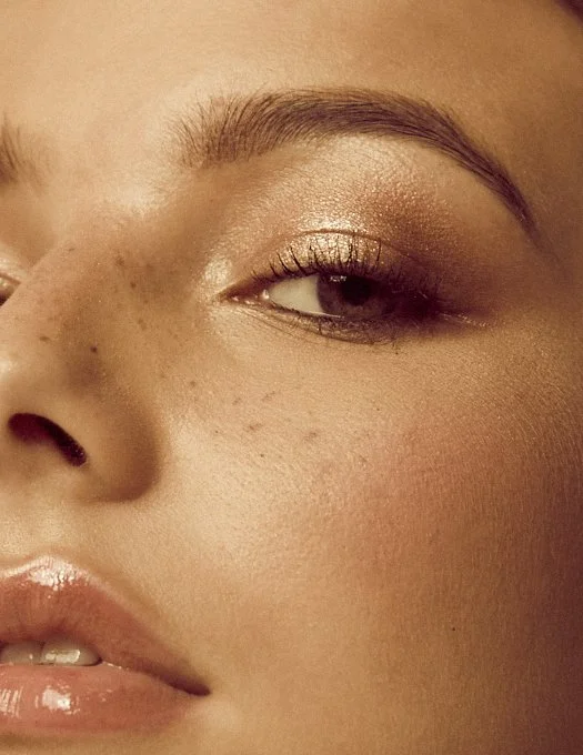 Close-up of a woman's face showing her eye, eyebrow, and part of her nose and lips with makeup and freckles.