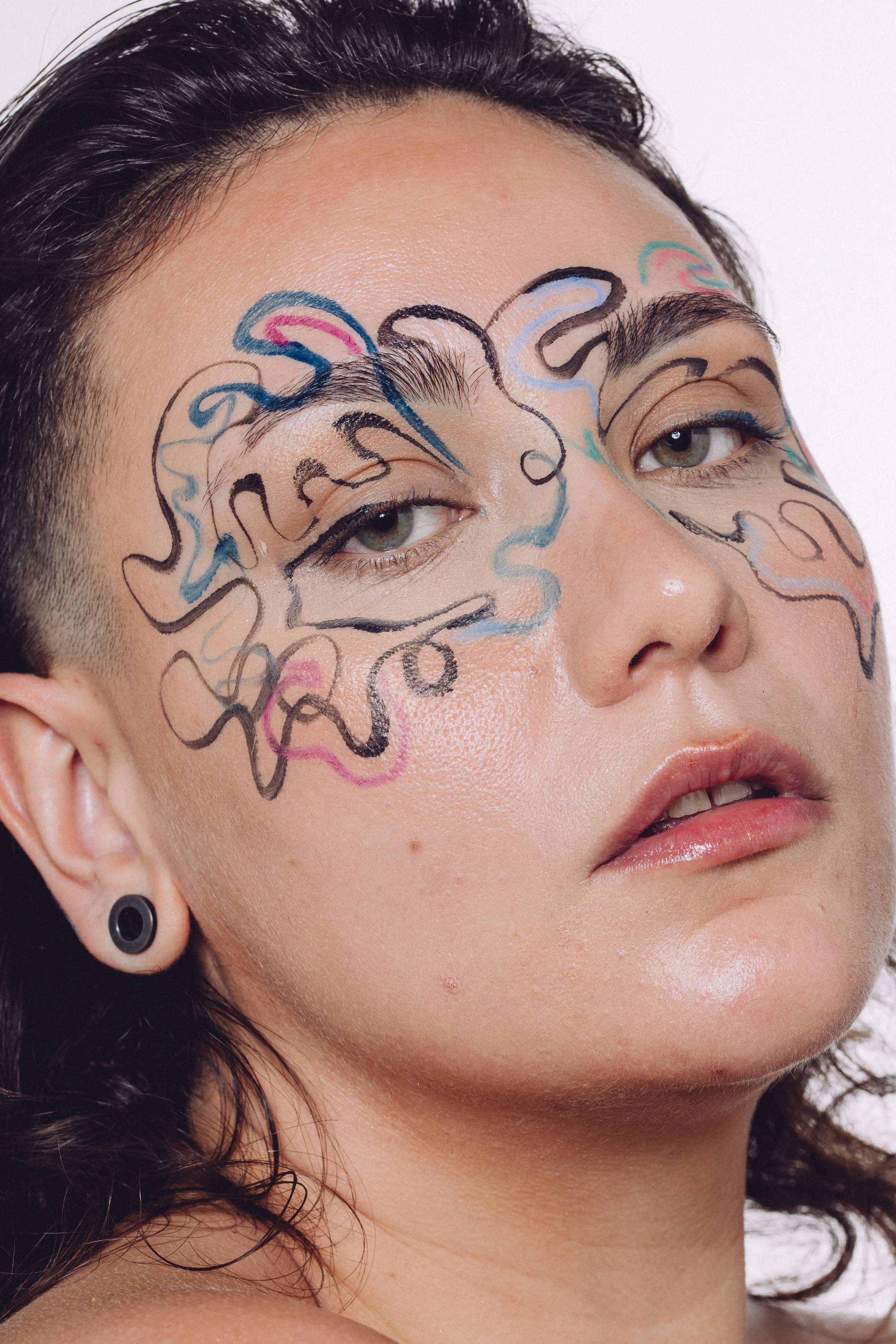 Close-up of a person with artistic, colorful face paint around the eyes, with a neutral facial expression.
