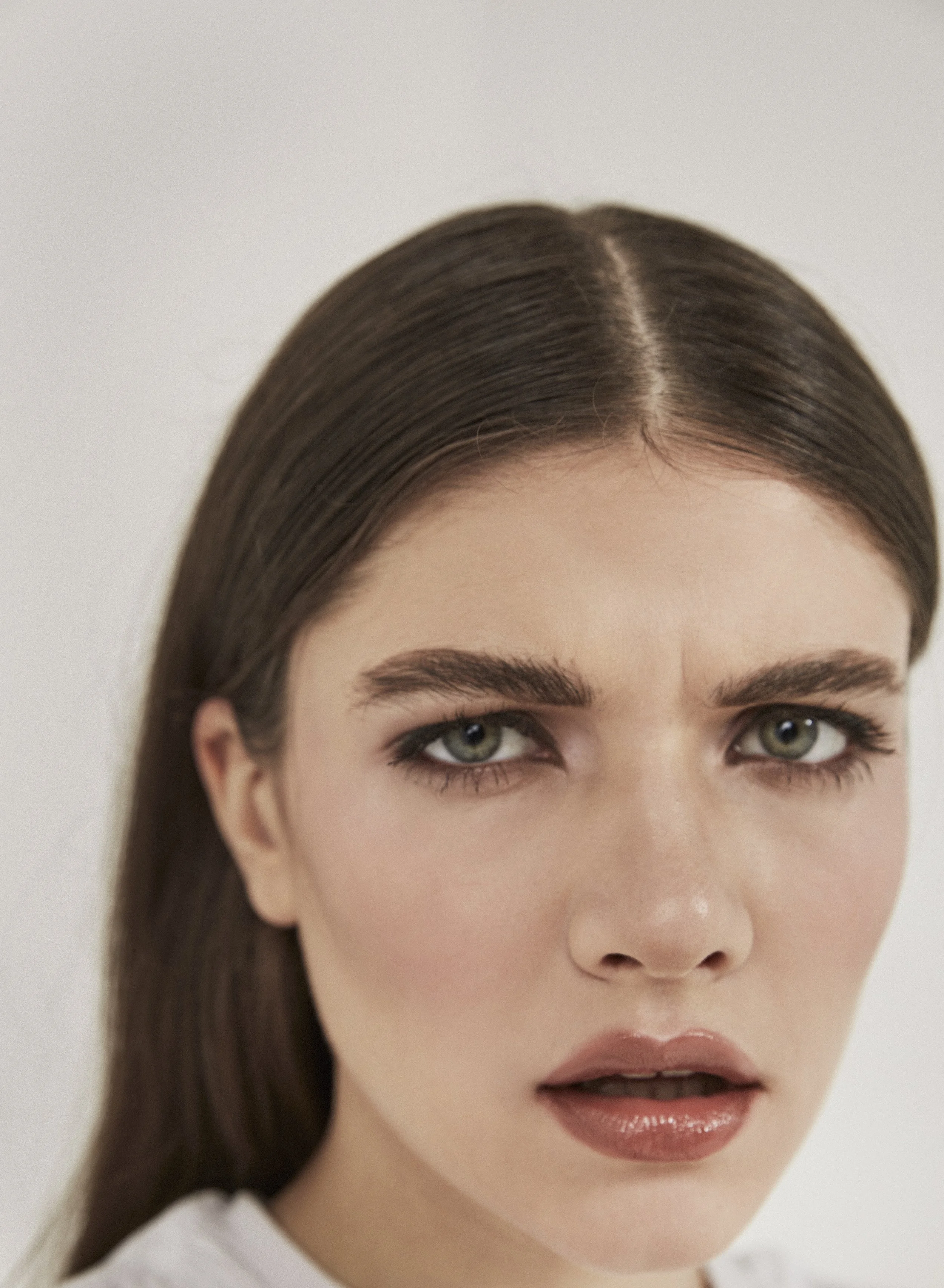 Close-up of a woman with long brown hair, green eyes, and a serious expression against a plain white background.