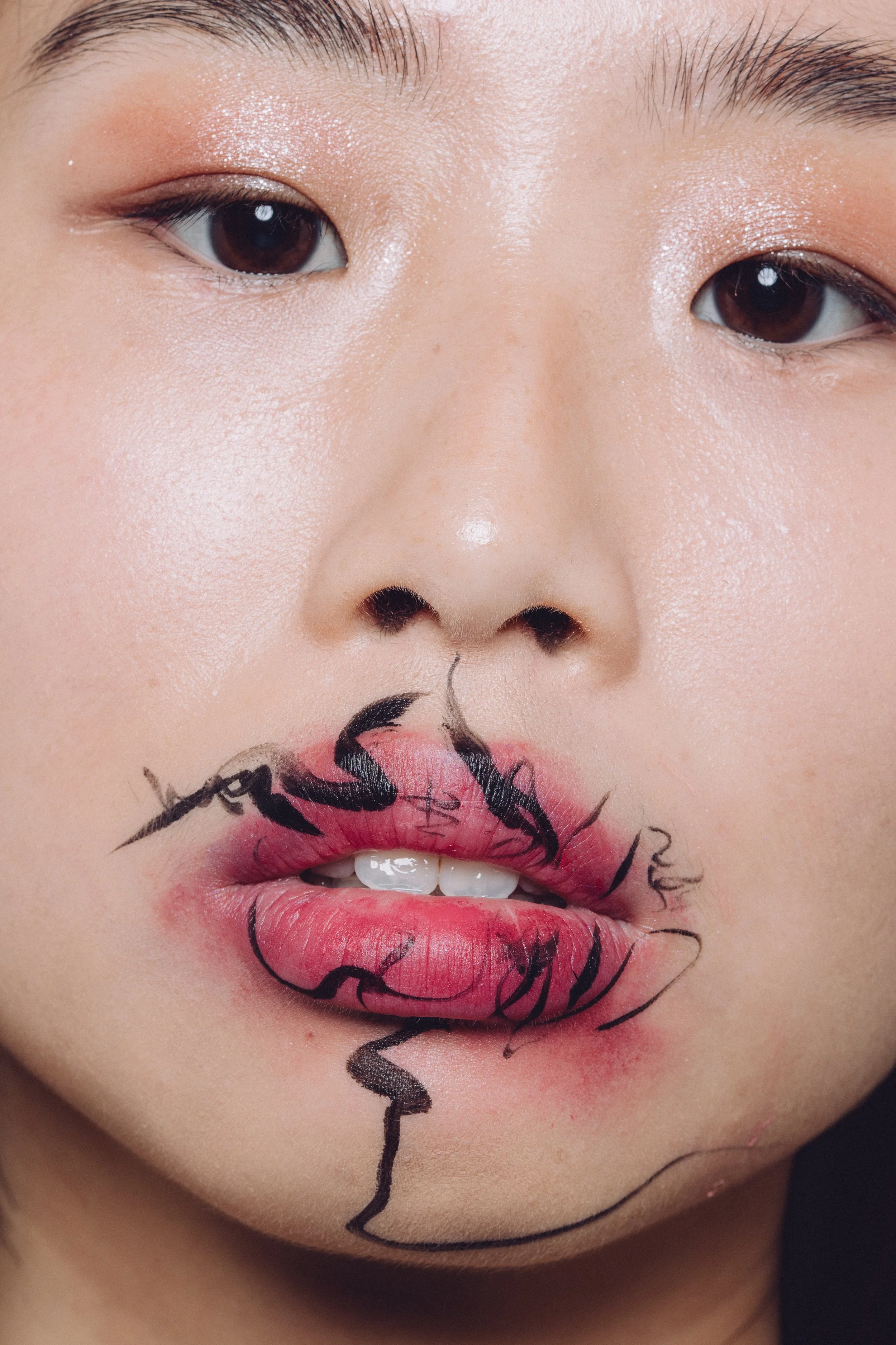 Close-up of a woman's face with artistic makeup, including drawn black lines and pink coloring on her lips.