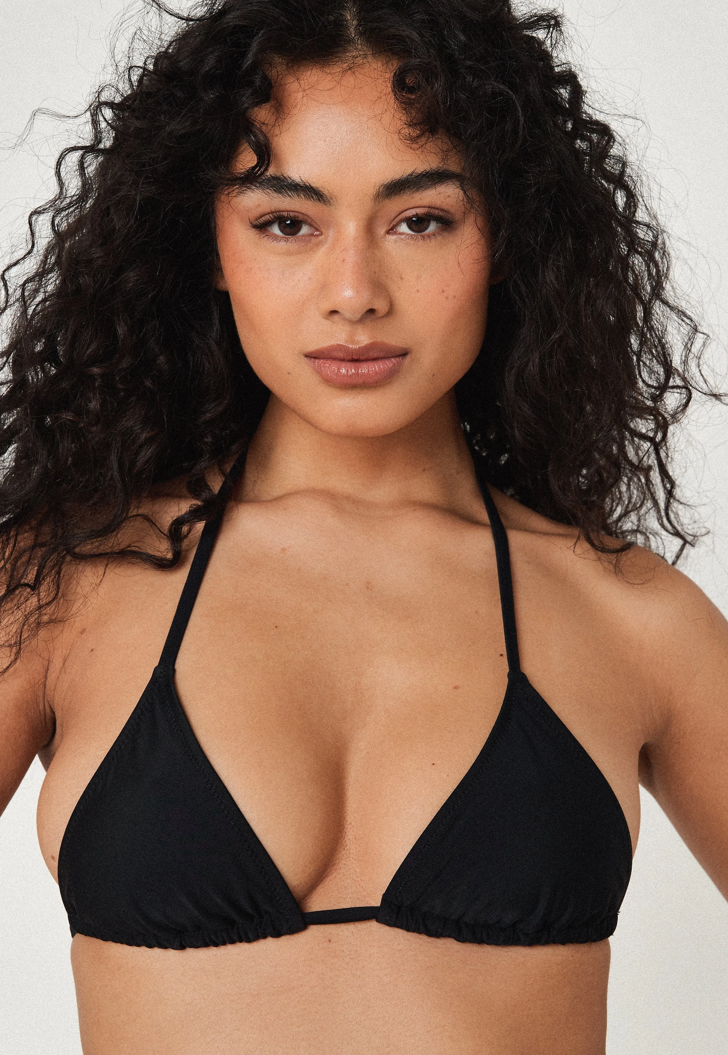 A young woman with curly dark hair wearing a black bikini top.