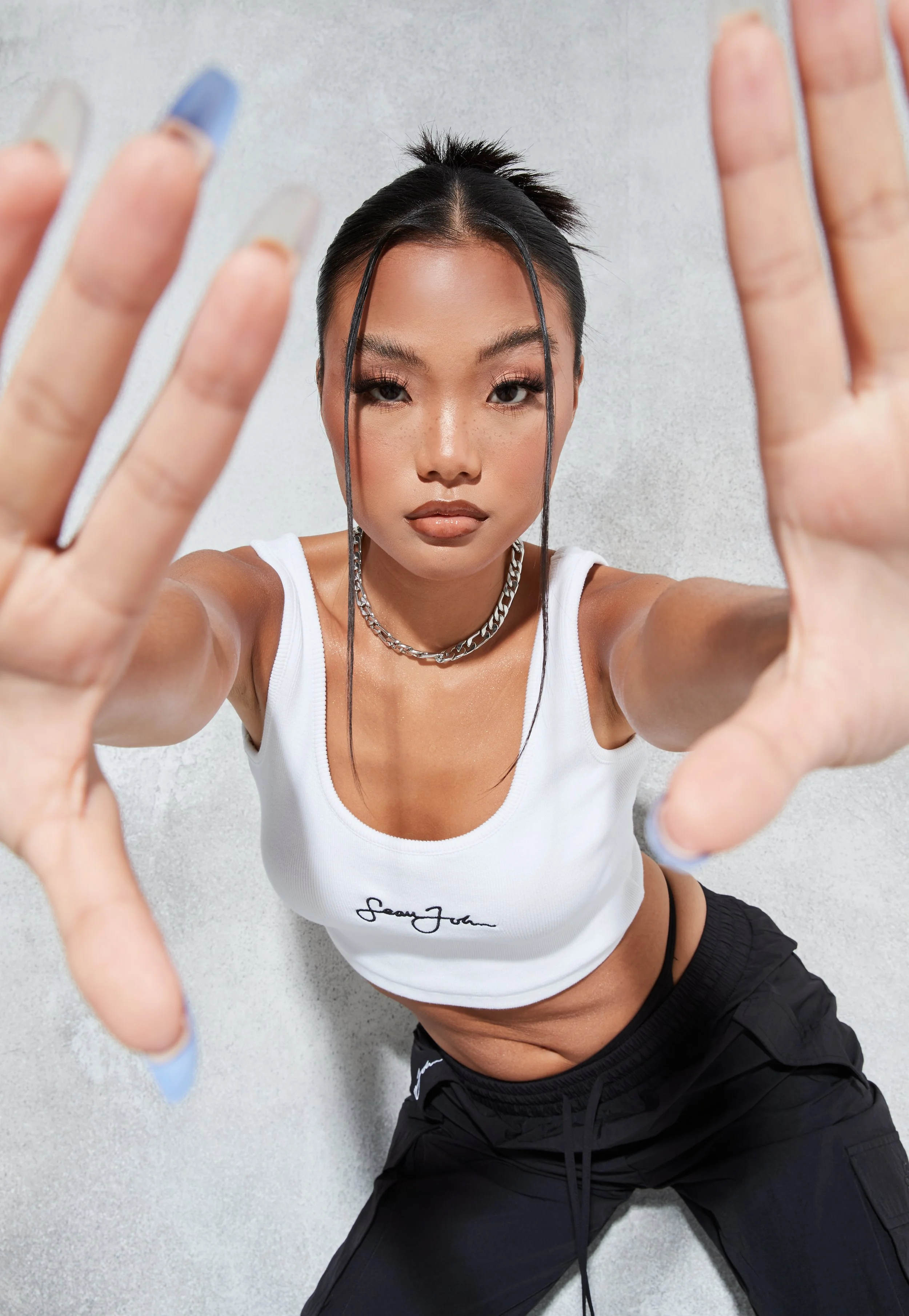 A woman in athletic clothing reaching toward the camera with both hands, looking directly at the lens with an intense expression.