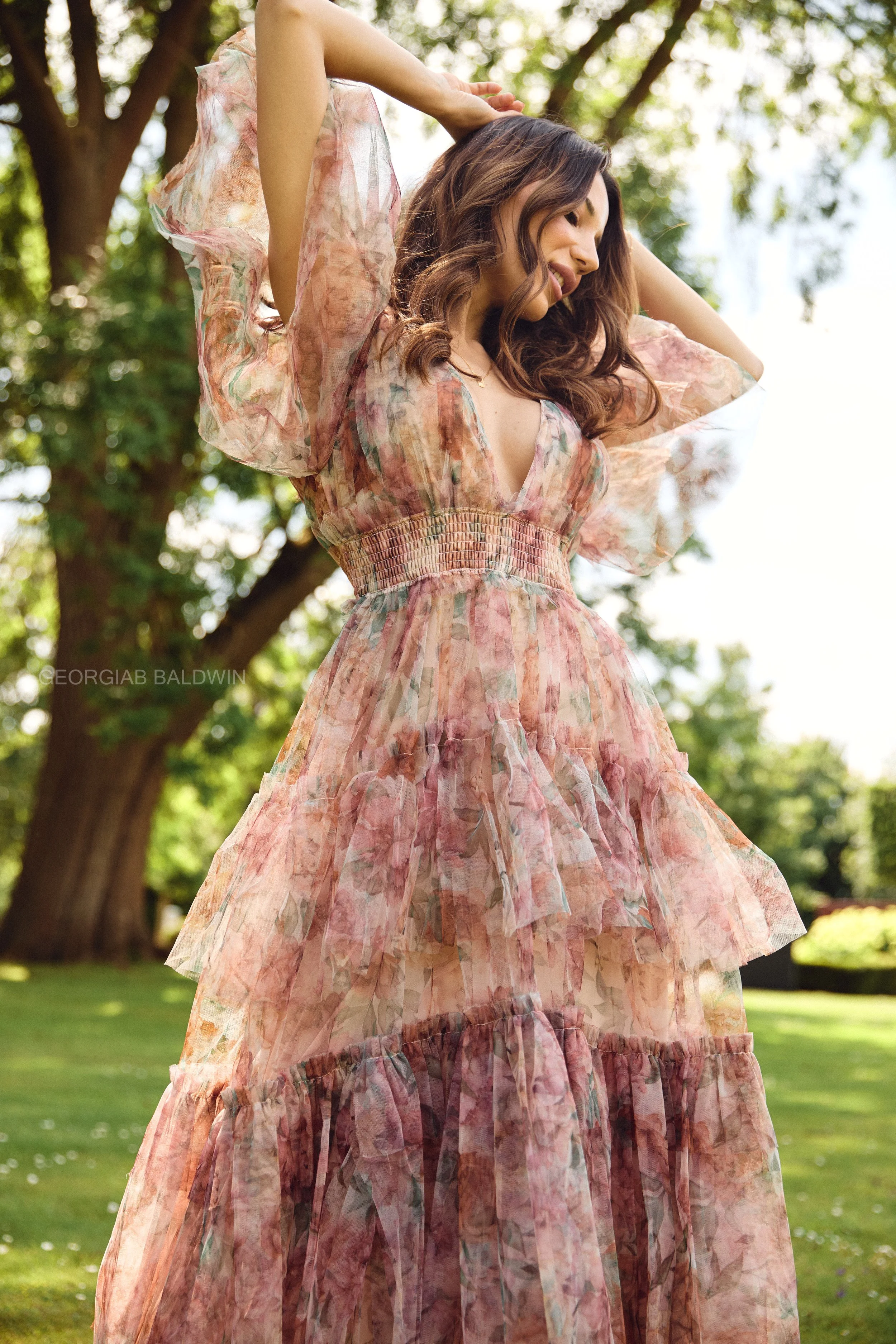 A woman wearing a flowy, pastel-colored, abstract-pattern dress outdoors with trees in the background.