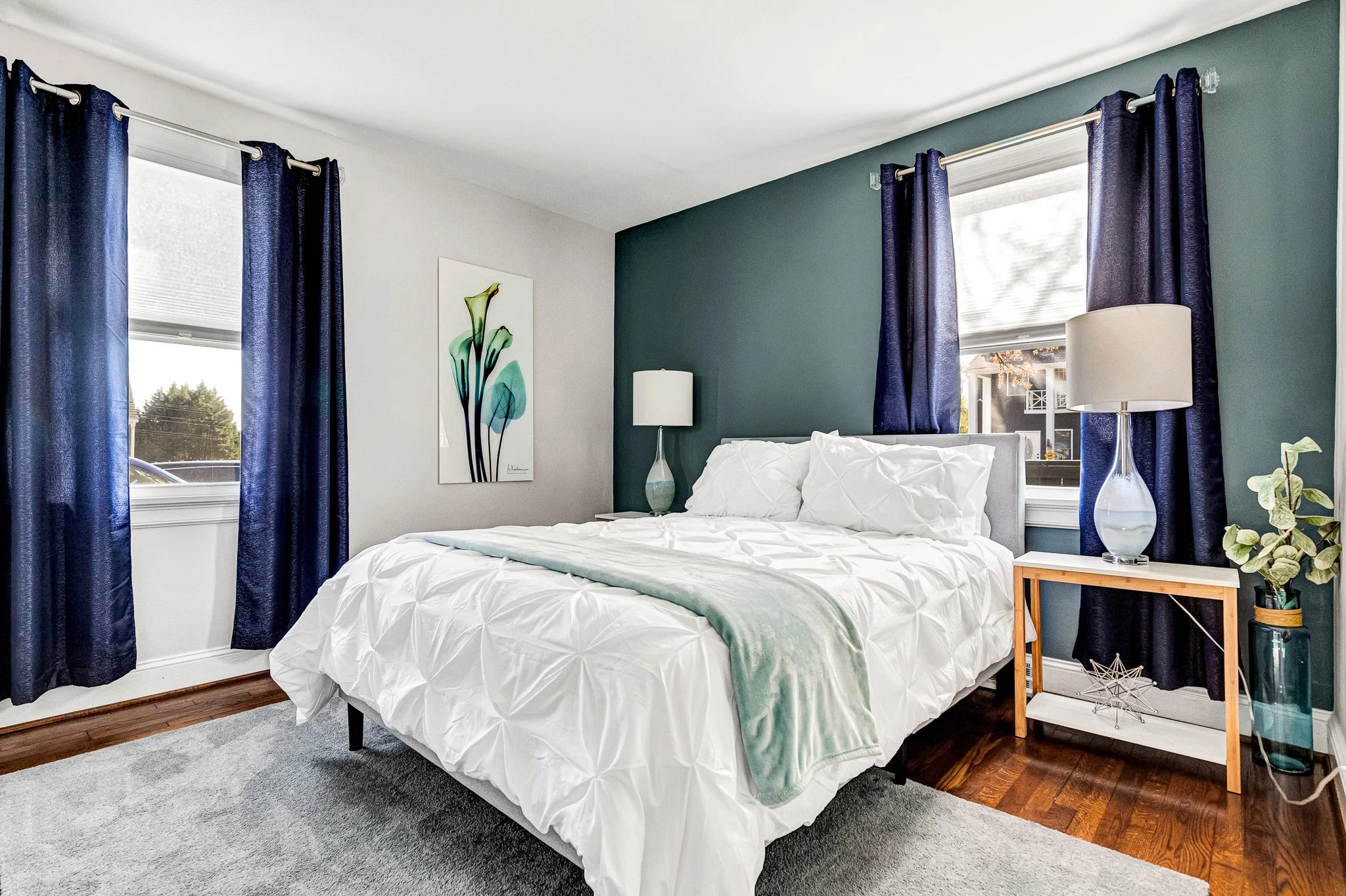 Queen bedroom with rich teal accent wall, luxury white linens, and a calm, beautifully appointed atmosphere.