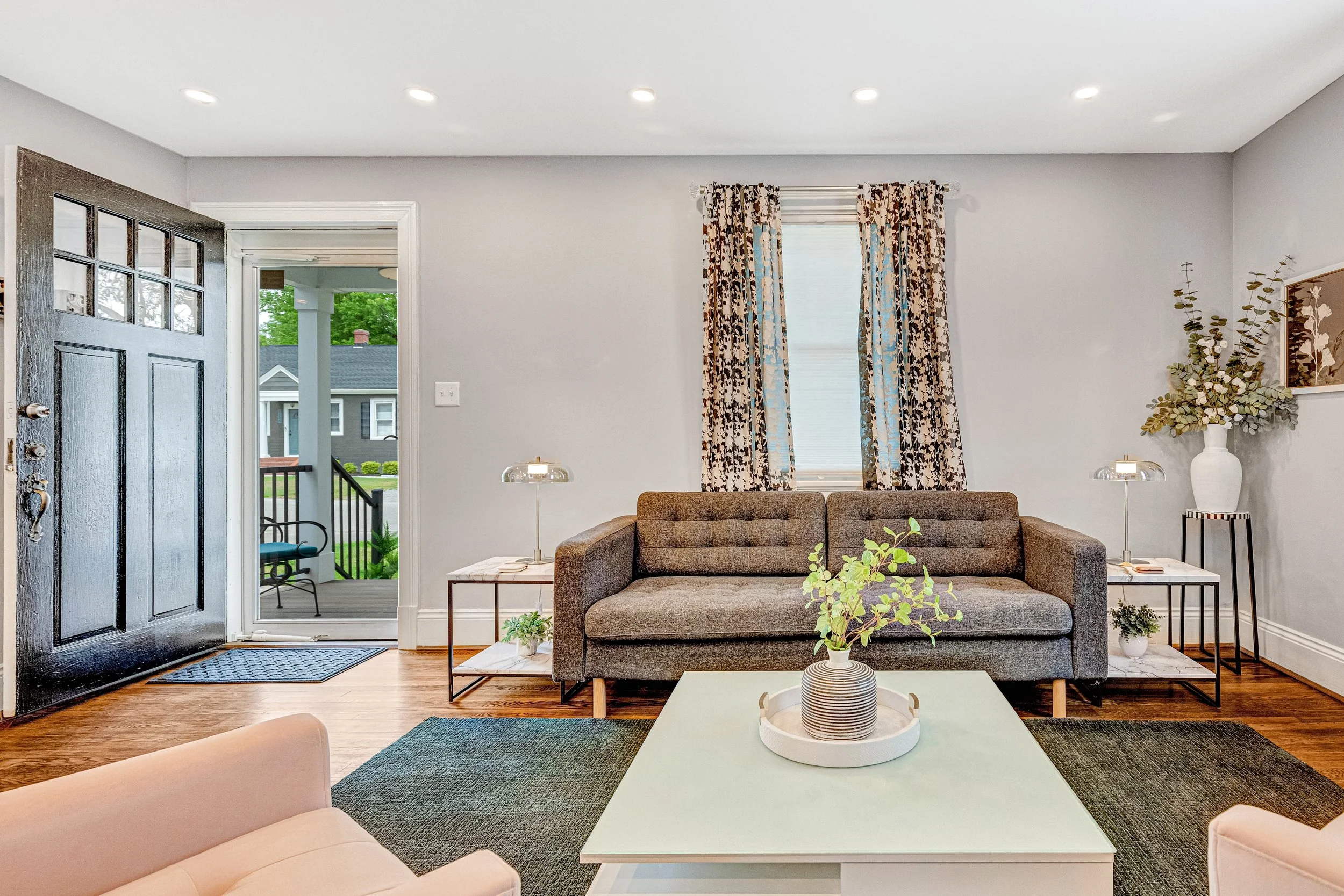 The living room features a modern couch, pink armchairs, a coffee table and large, sunny windows.