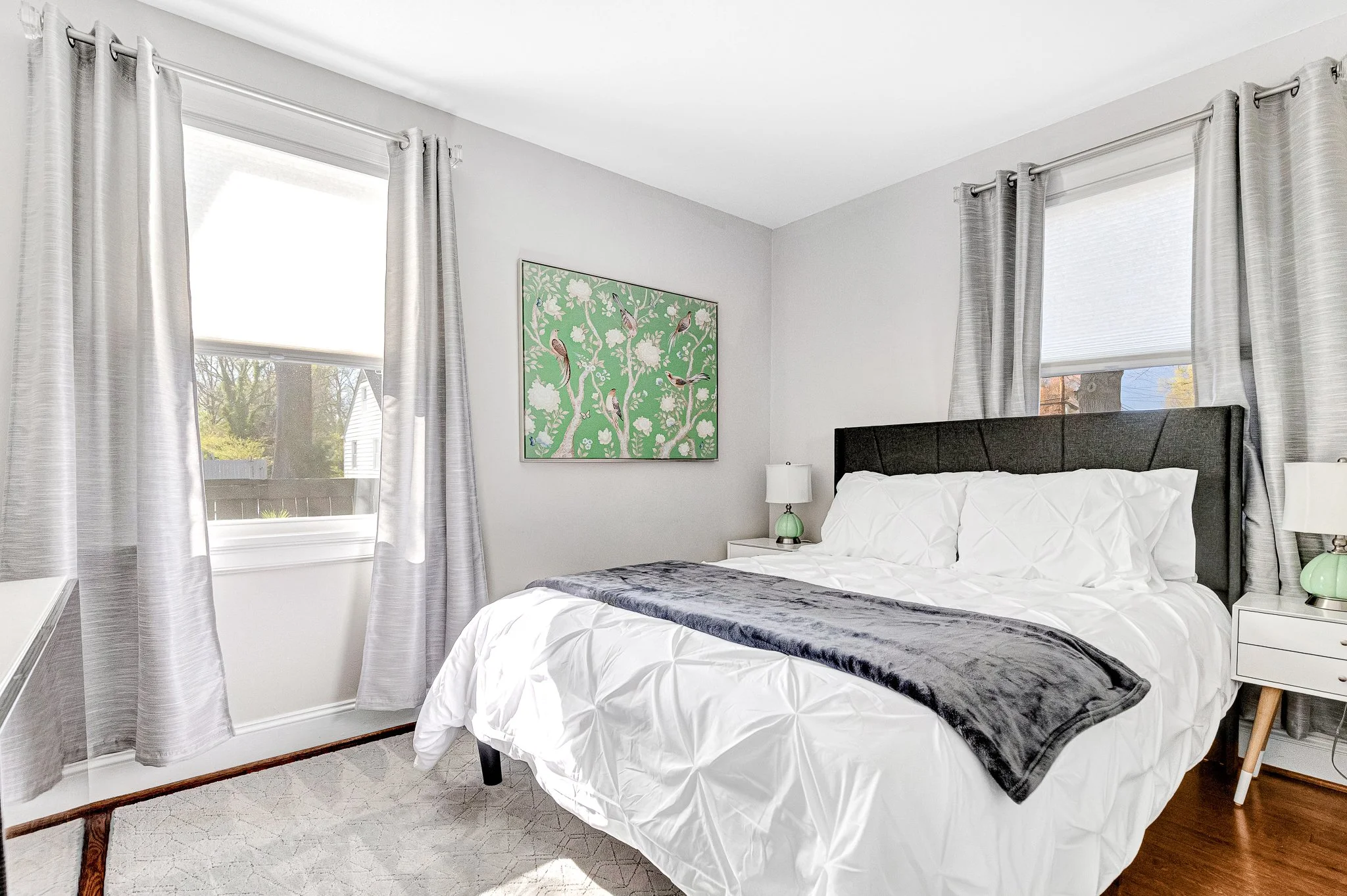 Sun-filled queen bedroom with large windows and fresh botanical artwork, calm and relaxing.