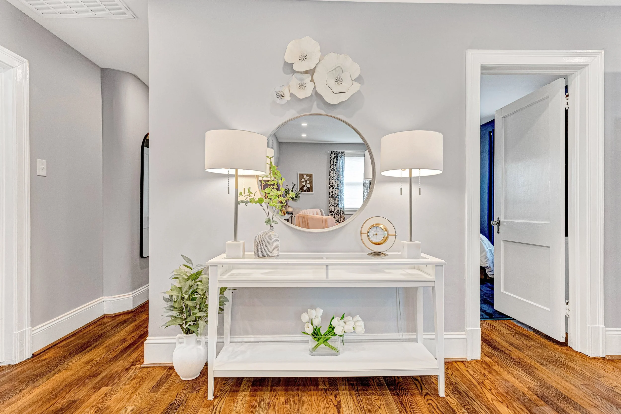 Designer entryway with a gold clock, mirror and elegant lamps.