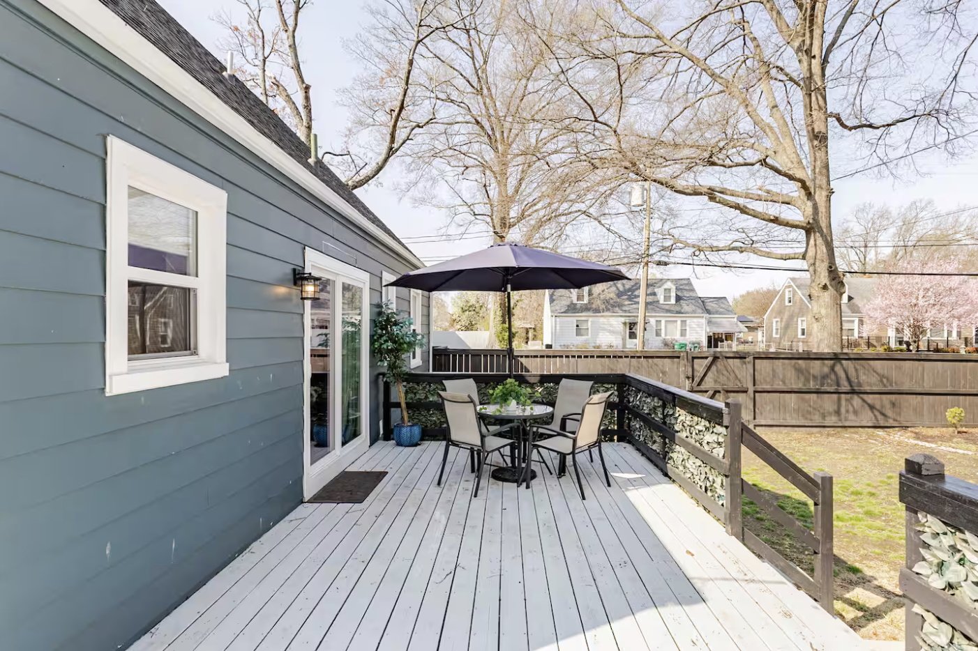 Sunny deck with outdoor dining table and umbrella, opening to a fully fenced backyard ideal for pets, kids, and weekend gatherings.