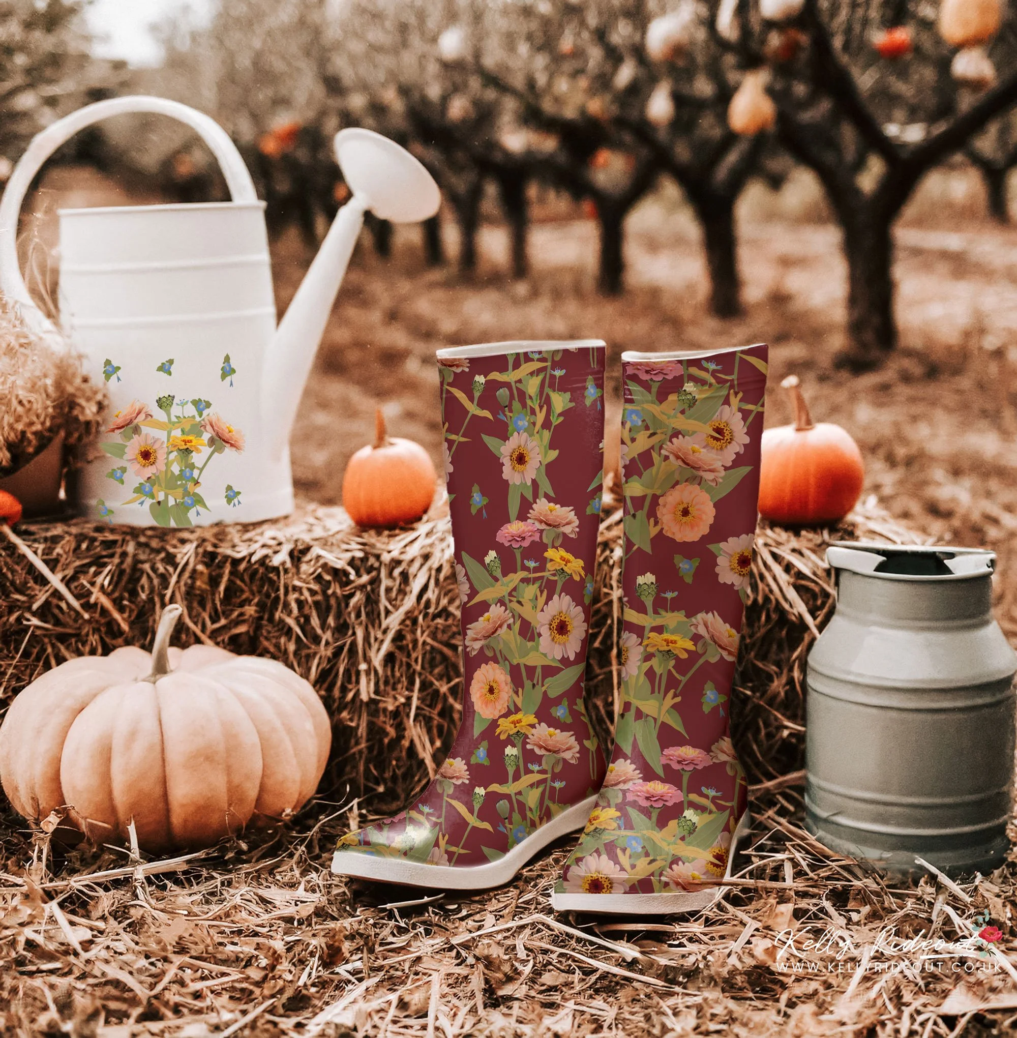 A pair of tall, floral-patterned rain boots standing on autumn leaves, surrounded by pumpkins, a watering can, and a gray container, with an orchard of trees in the background. Example of Kelly Rideout's patterns for licensing  on wellie boots