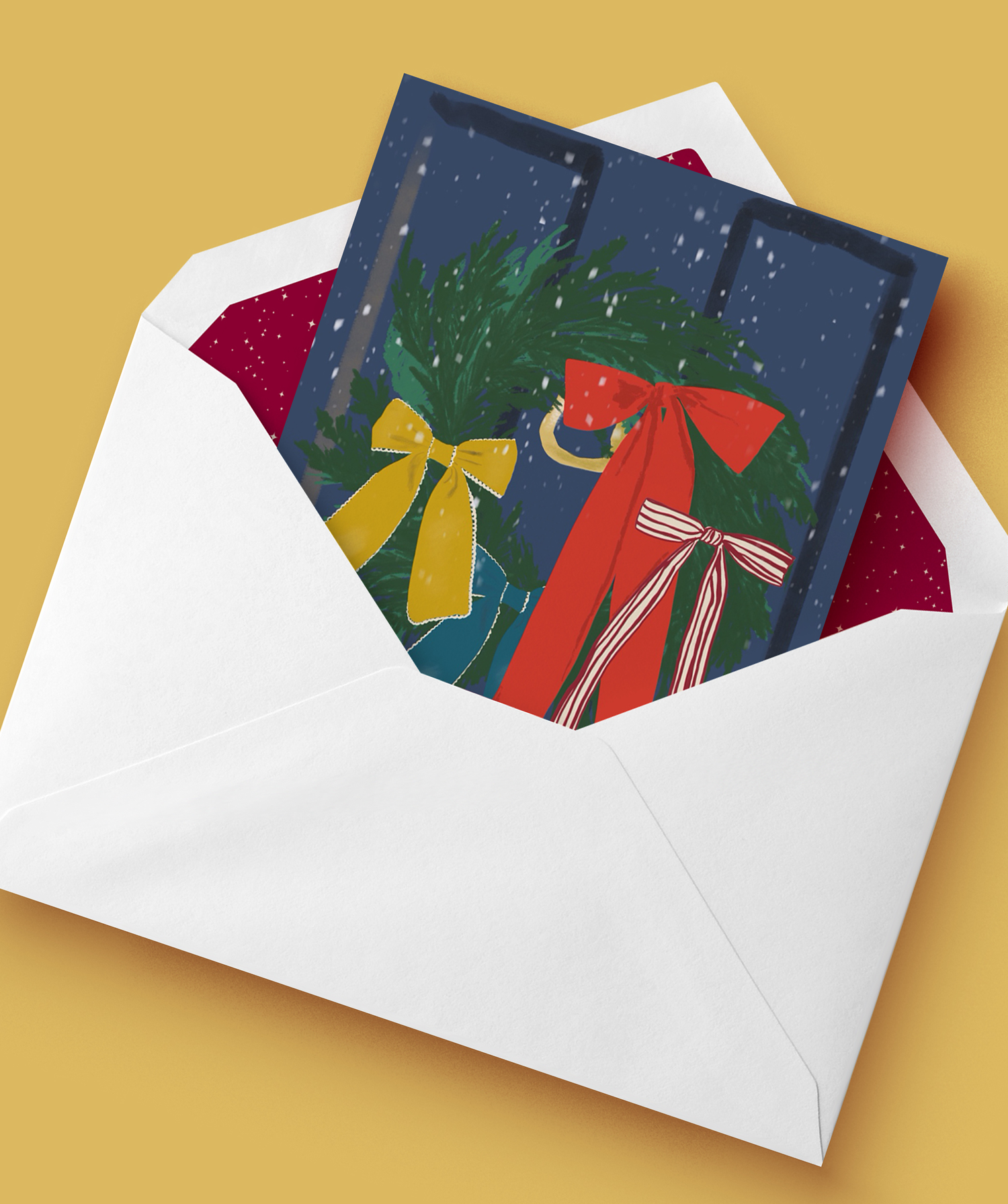 A white envelope contains a Christmas card with green wreaths decorated with red and yellow ribbons and snow falling against a dark background.
