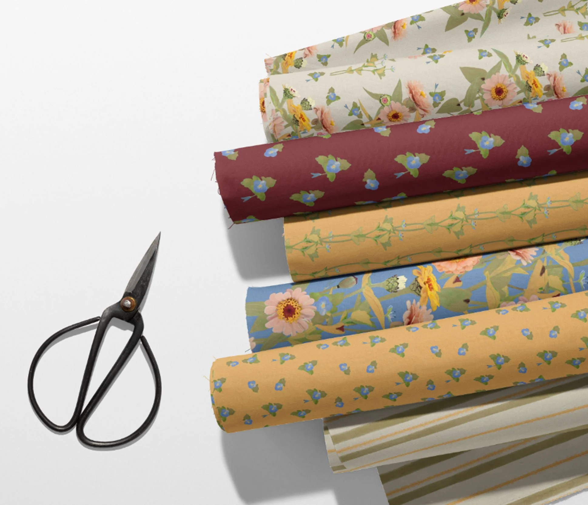Five rolls of floral and striped wrapping paper and a pair of black scissors on a white surface.