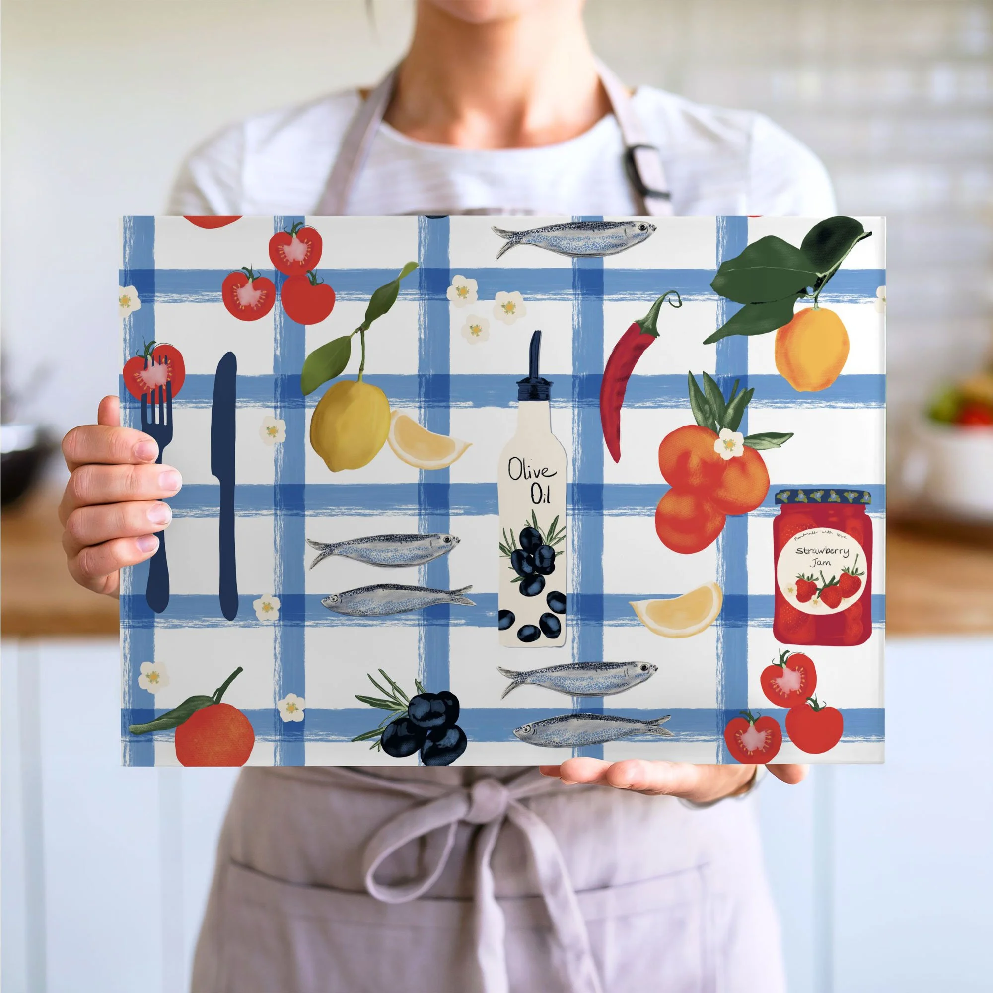 Person holding a colorful kitchen wall art with fruits, vegetables, fish, olive oil, and jam on a blue checkered background.