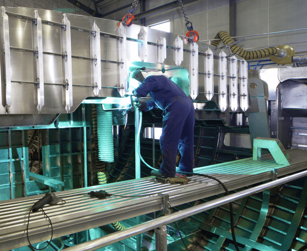 A worker in protective gear welding a large stainless steel industrial tank in a manufacturing facility.