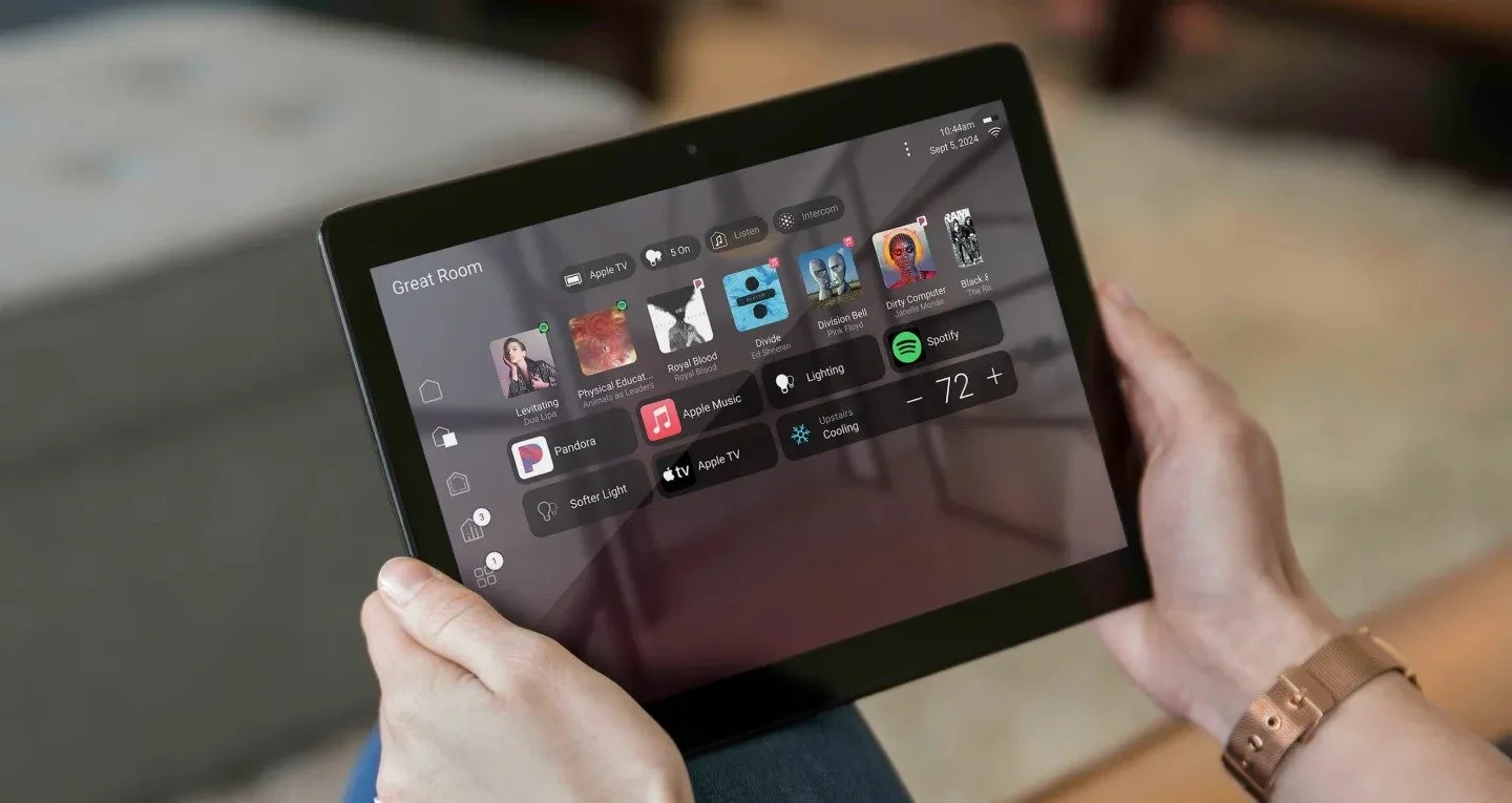 A person holding a tablet displaying a smart home control interface with app icons and settings.