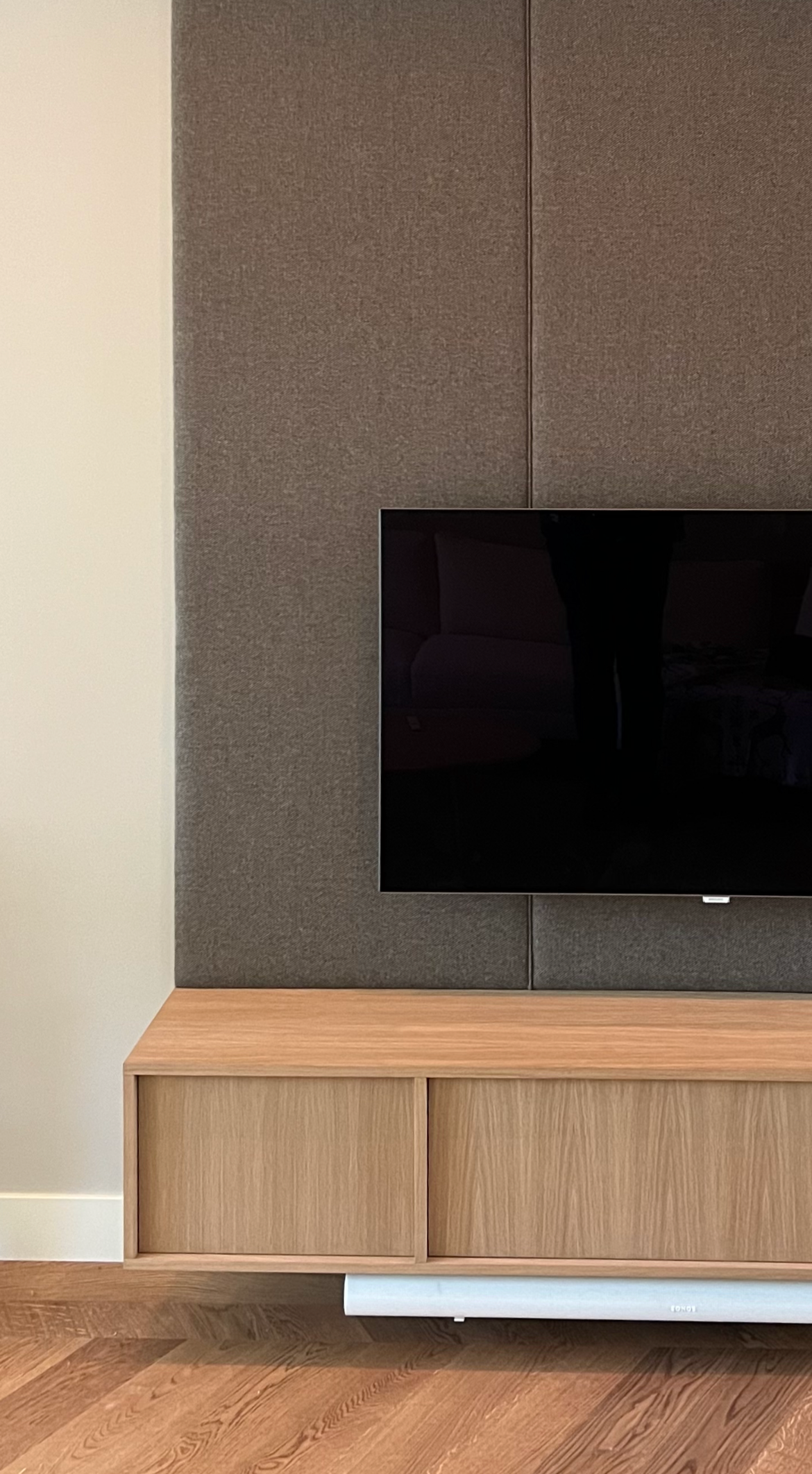 Een houten tv-meubel met een bekleedde wandpaneel achter de tv. Op maat gemaakt textiel akoestisch wandmeubel. Maatwerk Den Haag.