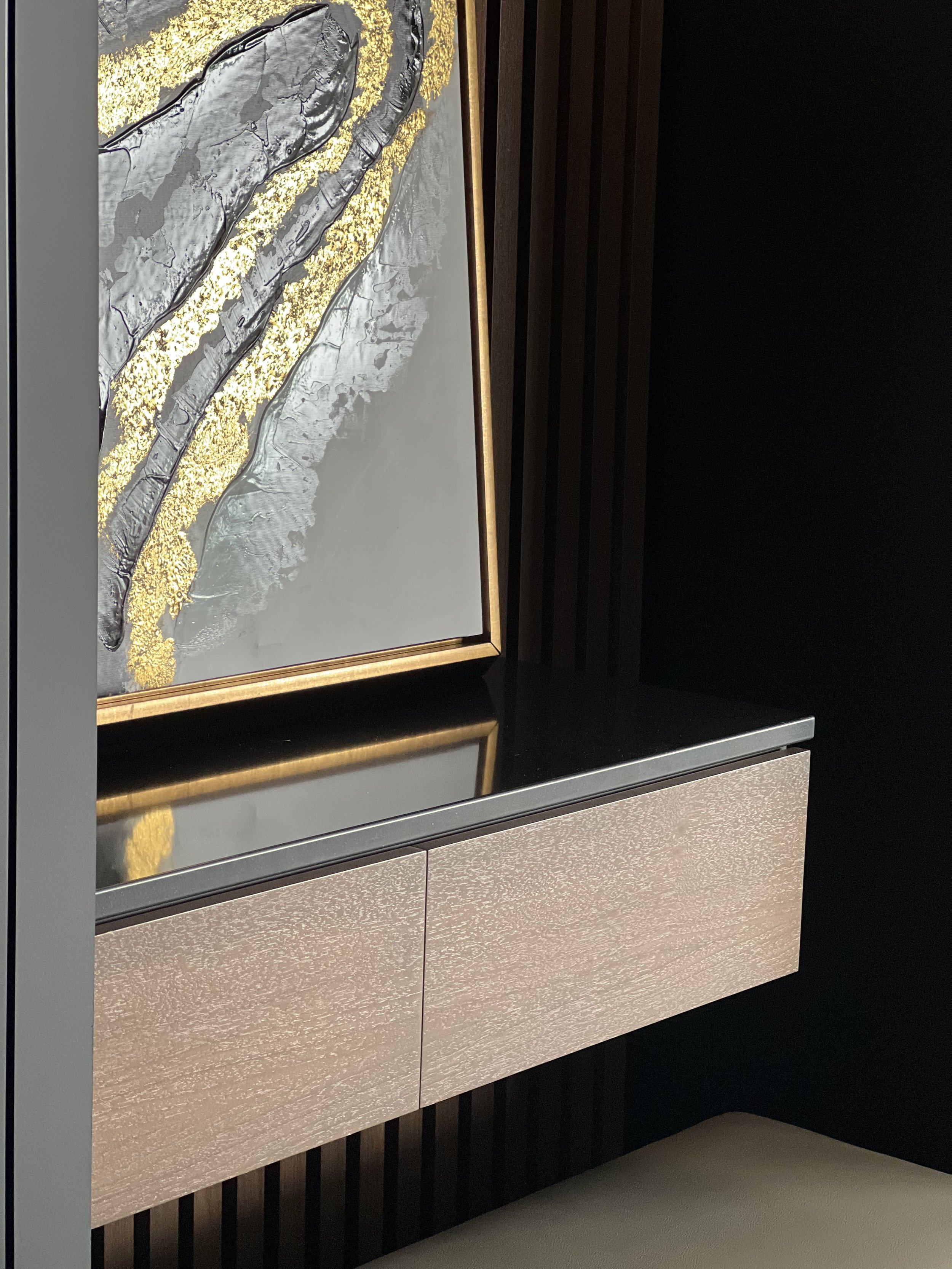 Close-up of a modern interior with a textured beige cabinet, black reflective surface, and a gold and silver abstract painting on the wall.