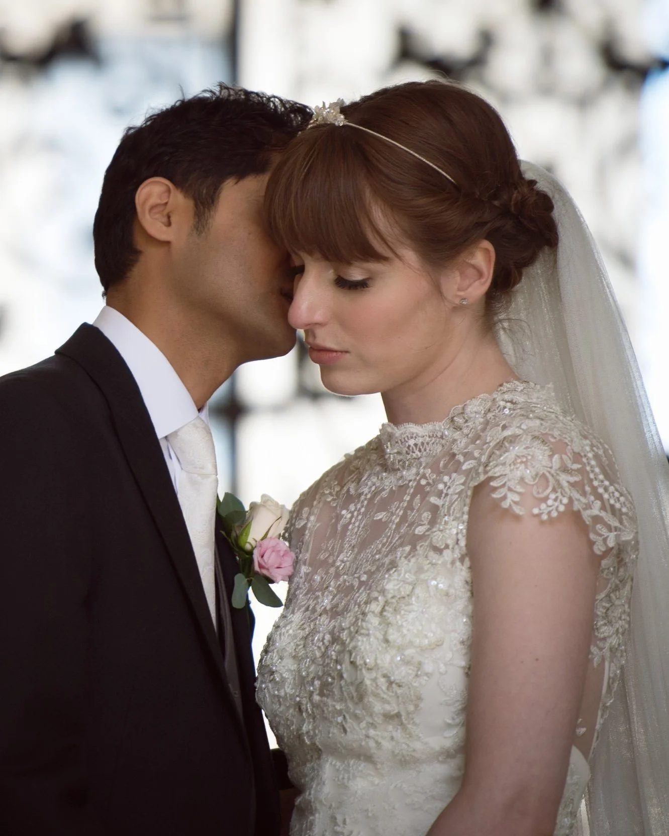 Wedding portrait groom kissing bride front of a gate in oxford