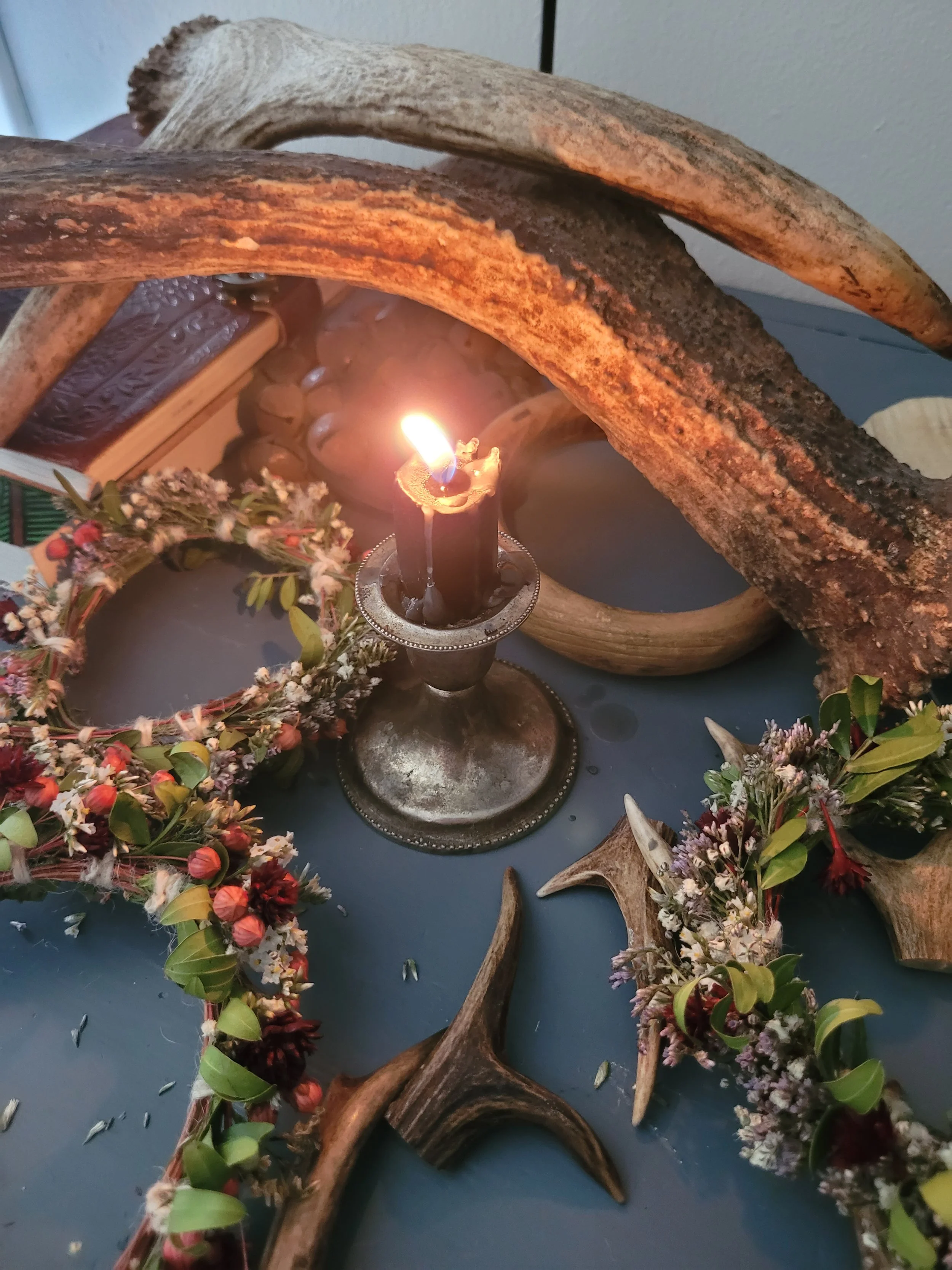 Arrangement of antlers, flowers, and a lit candle on a table.
