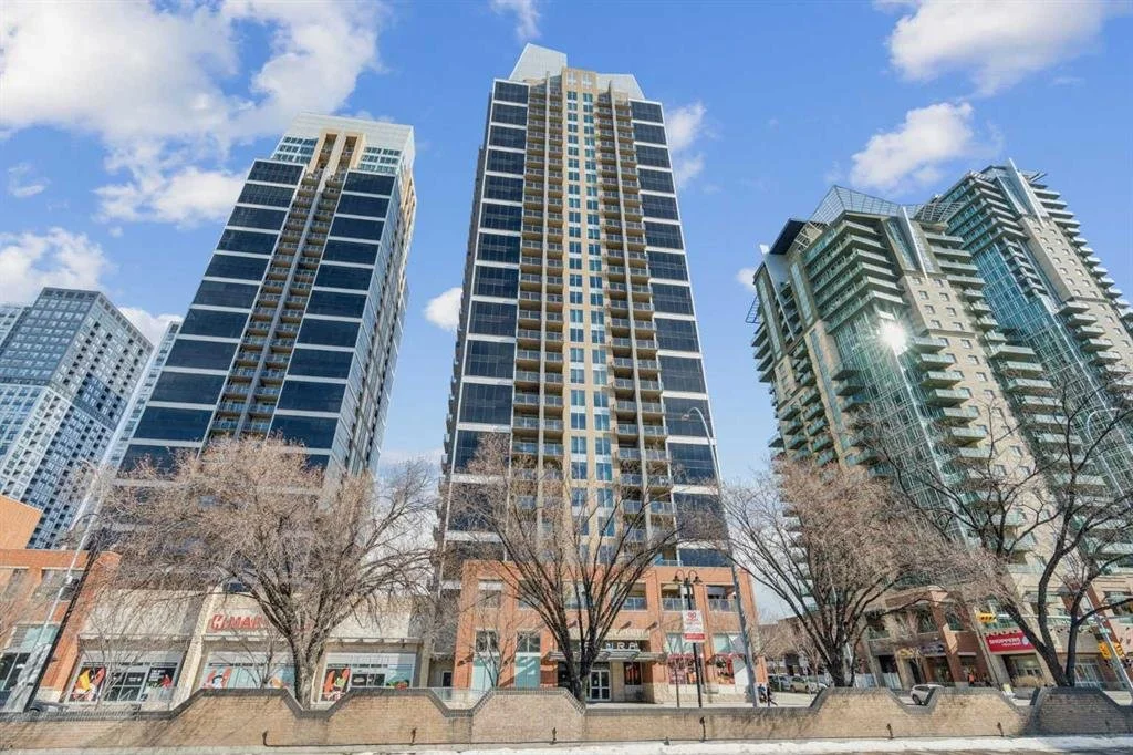 Tall modern high-rise buildings in a cityscape under a partly cloudy sky, with some trees and a street in the foreground.