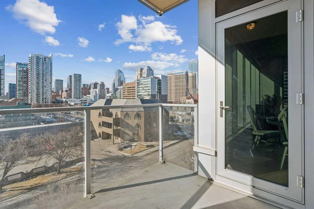 Balcony with glass railing overlooking a city skyline with tall buildings under a partly cloudy sky.