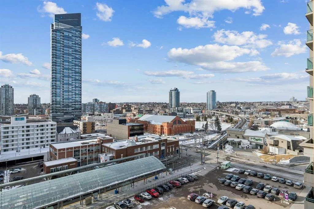 Cityscape with tall modern skyscraper, mid-rise buildings, and a partly cloudy sky.