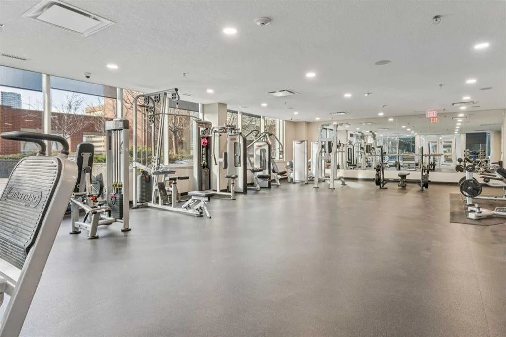 Empty gym with various workout equipment, large windows, and mirrors.